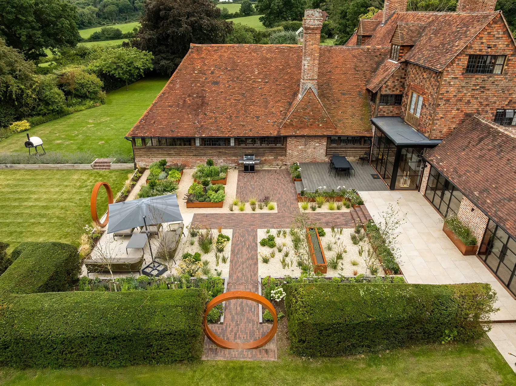 Aerial view of a house with a garden featuring neatly arranged flower beds, pathways, and lush greenery.