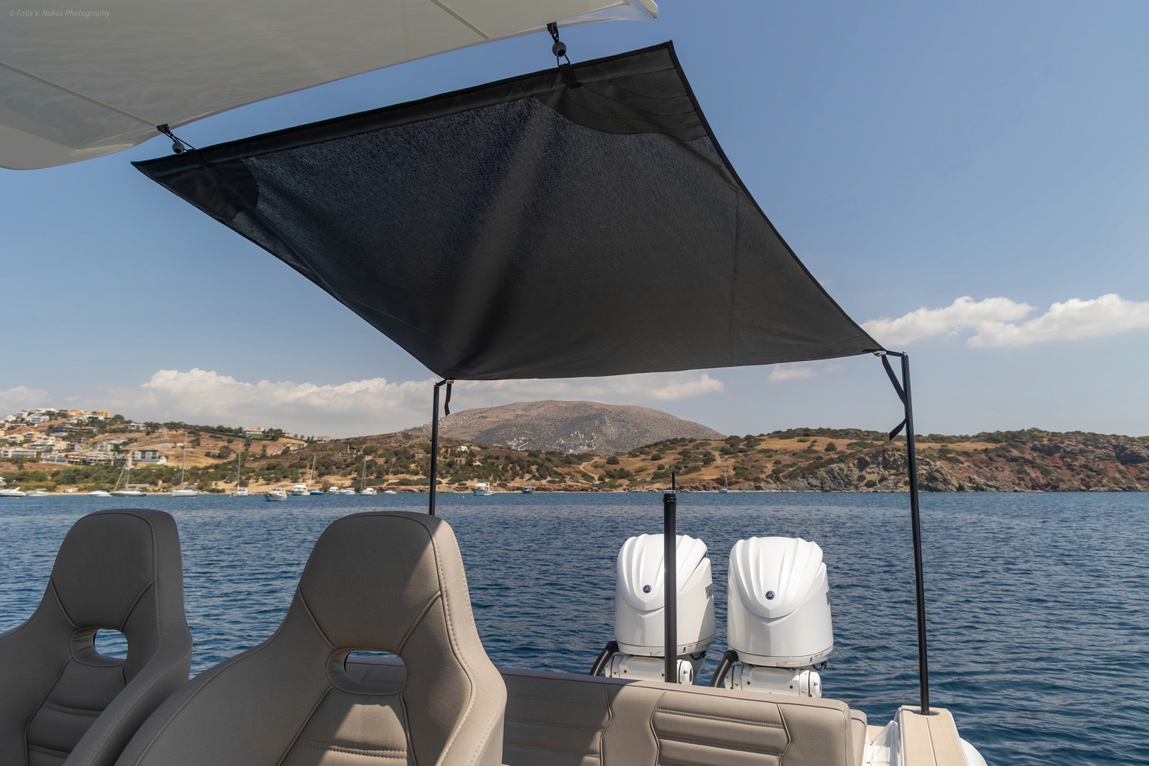 Shaded seating area on Rock 36 Naboo yacht deck with twin outboard engines, overlooking calm blue waters and Greek coastal hills.
