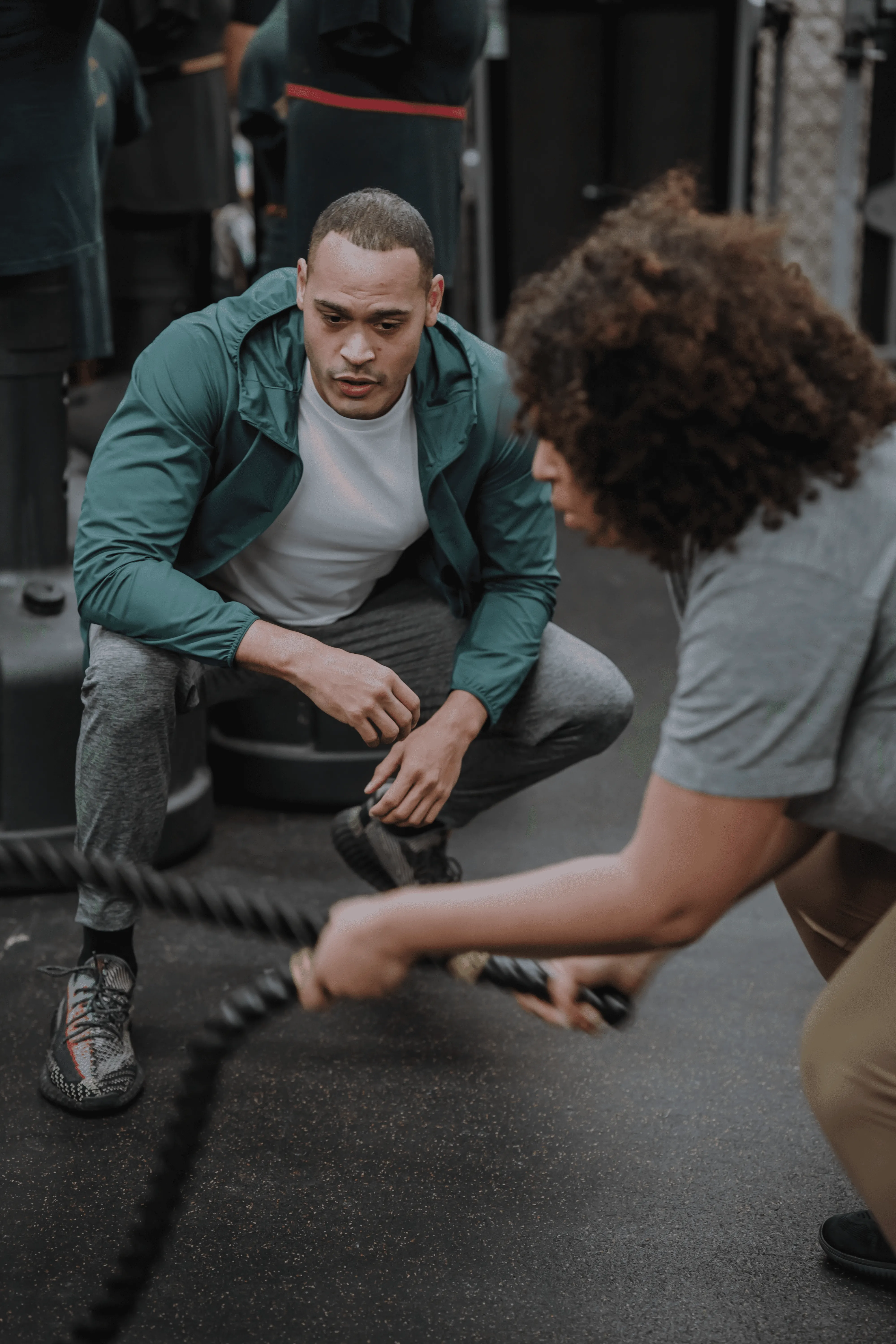 A pair of black dumbbells, a jump rope, and a water bottle are placed on a textured black workout mat, suggesting a home fitness session.