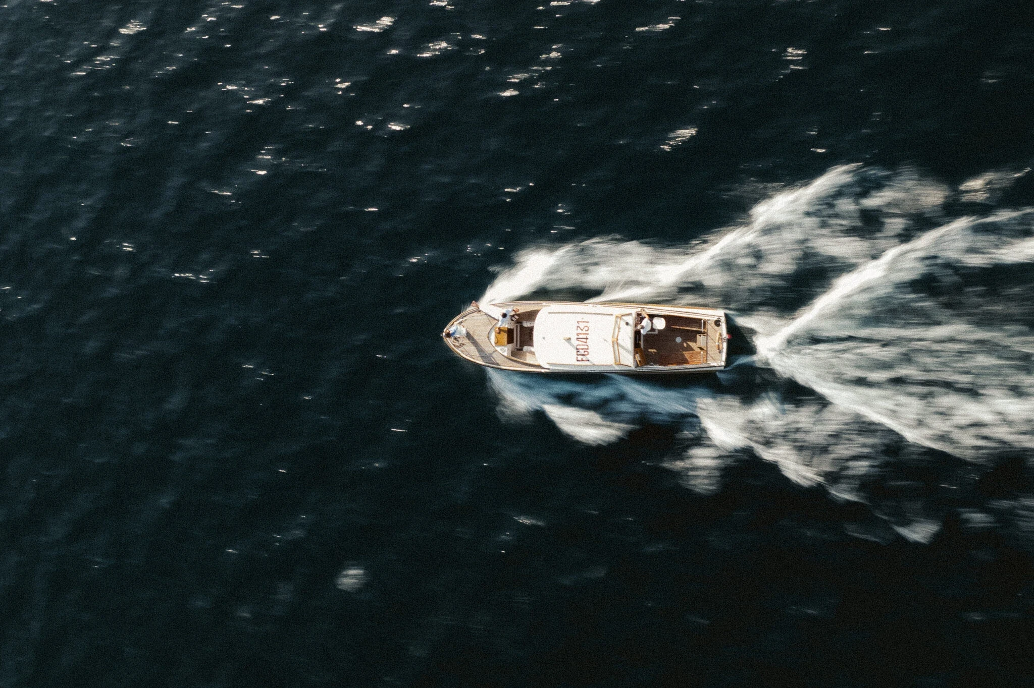 Draufsicht auf ein elegantes Speedboot aus Holz, das mit hoher Geschwindigkeit über das dunkelblaue Meer fährt und weiße Gischt im Wasser hinterlässt.