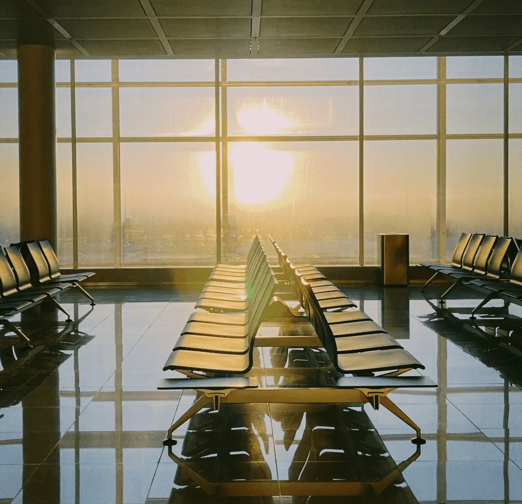 Rows of empty airport seats face large windows glowing at sunset.