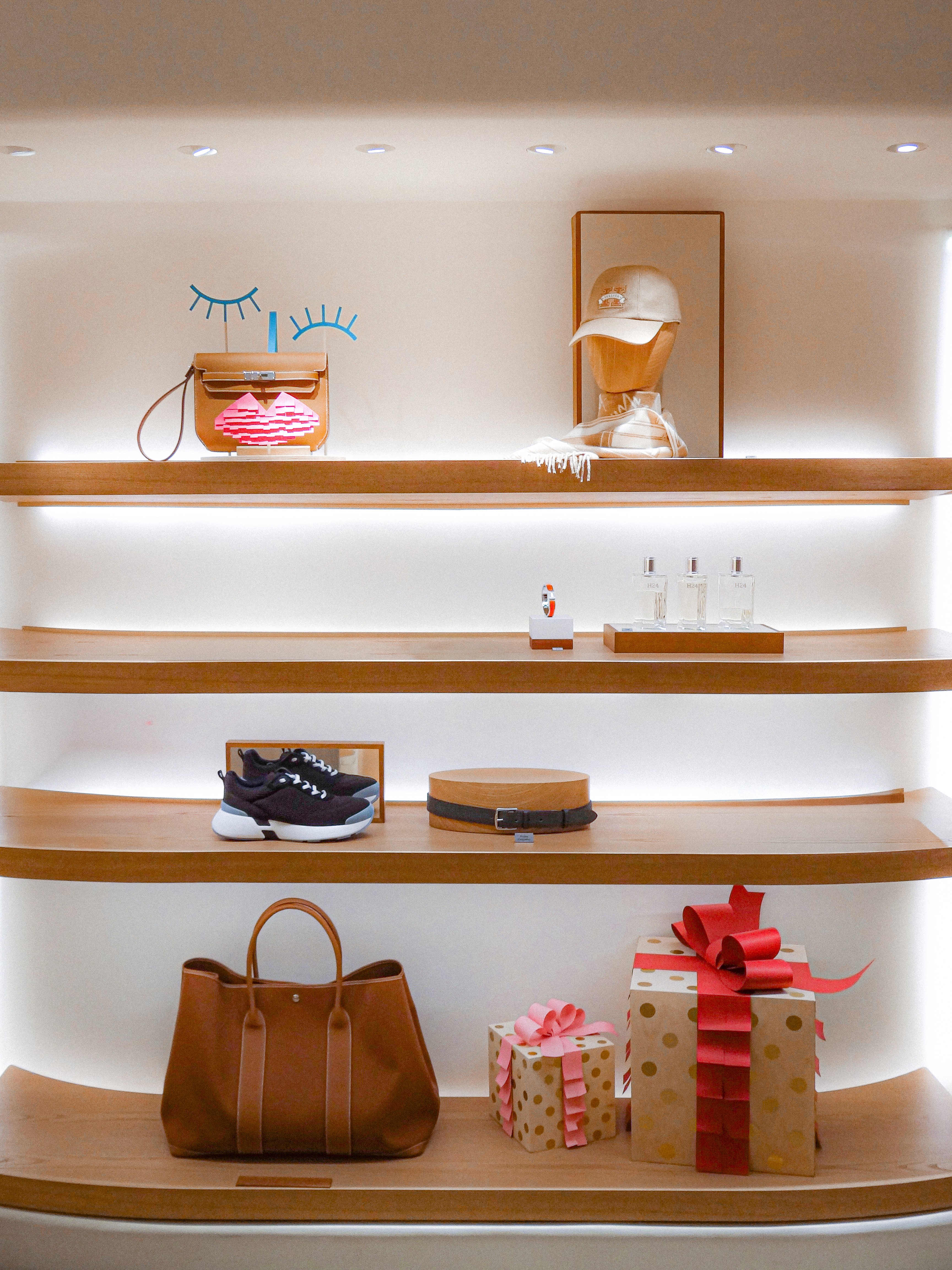 High-angle view of the Hermès holiday boutique interior, showcasing tiered shelving units featuring leather handbags, accessories, and fragrances integrated with playful character props and gold-dotted gift boxes, designed by WM Paris.