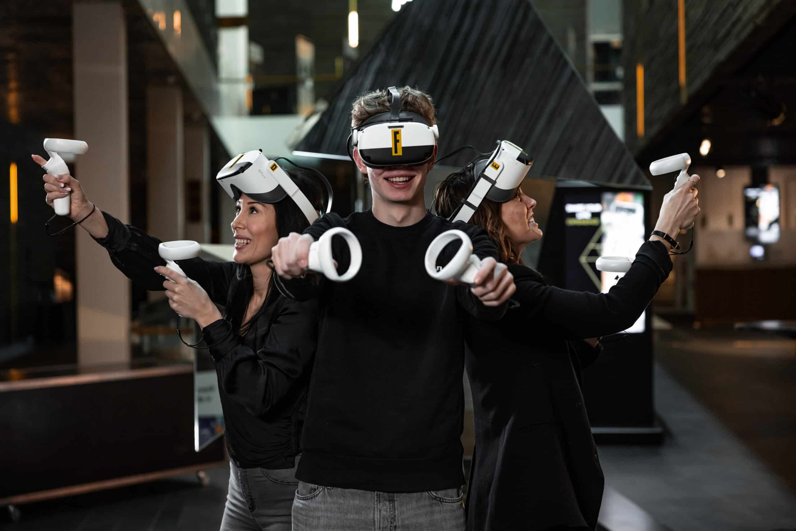 A young person with curly hair smiles at the camera while sitting in front of a laptop against a dark background.