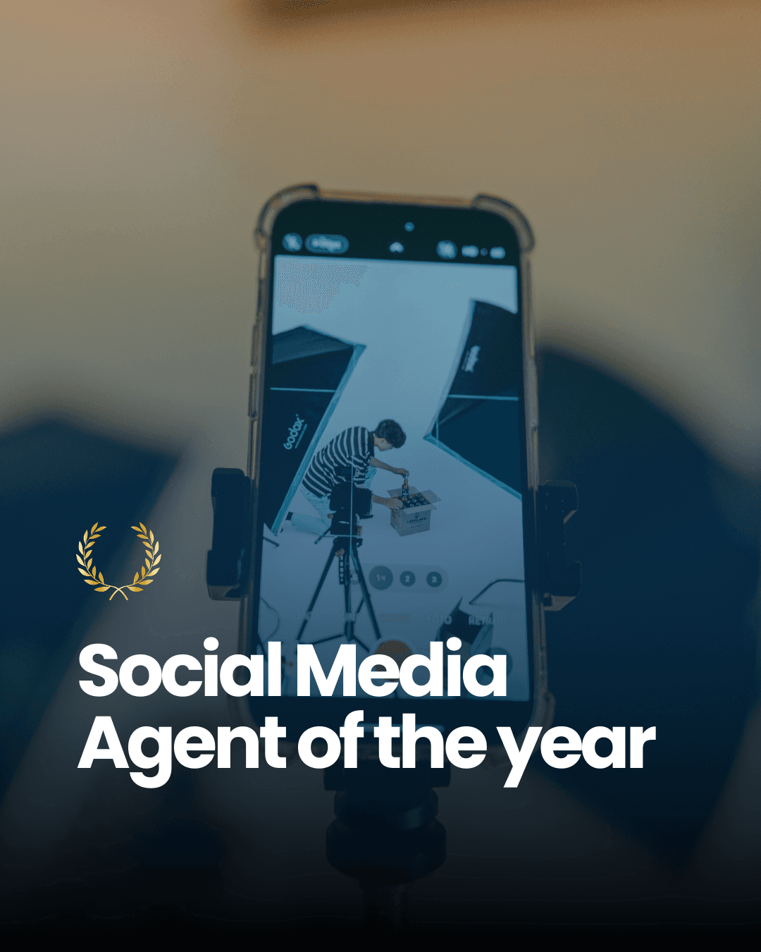 A smiling young man with crossed arms, wearing a plaid shirt and white t-shirt, poses against a dark background.