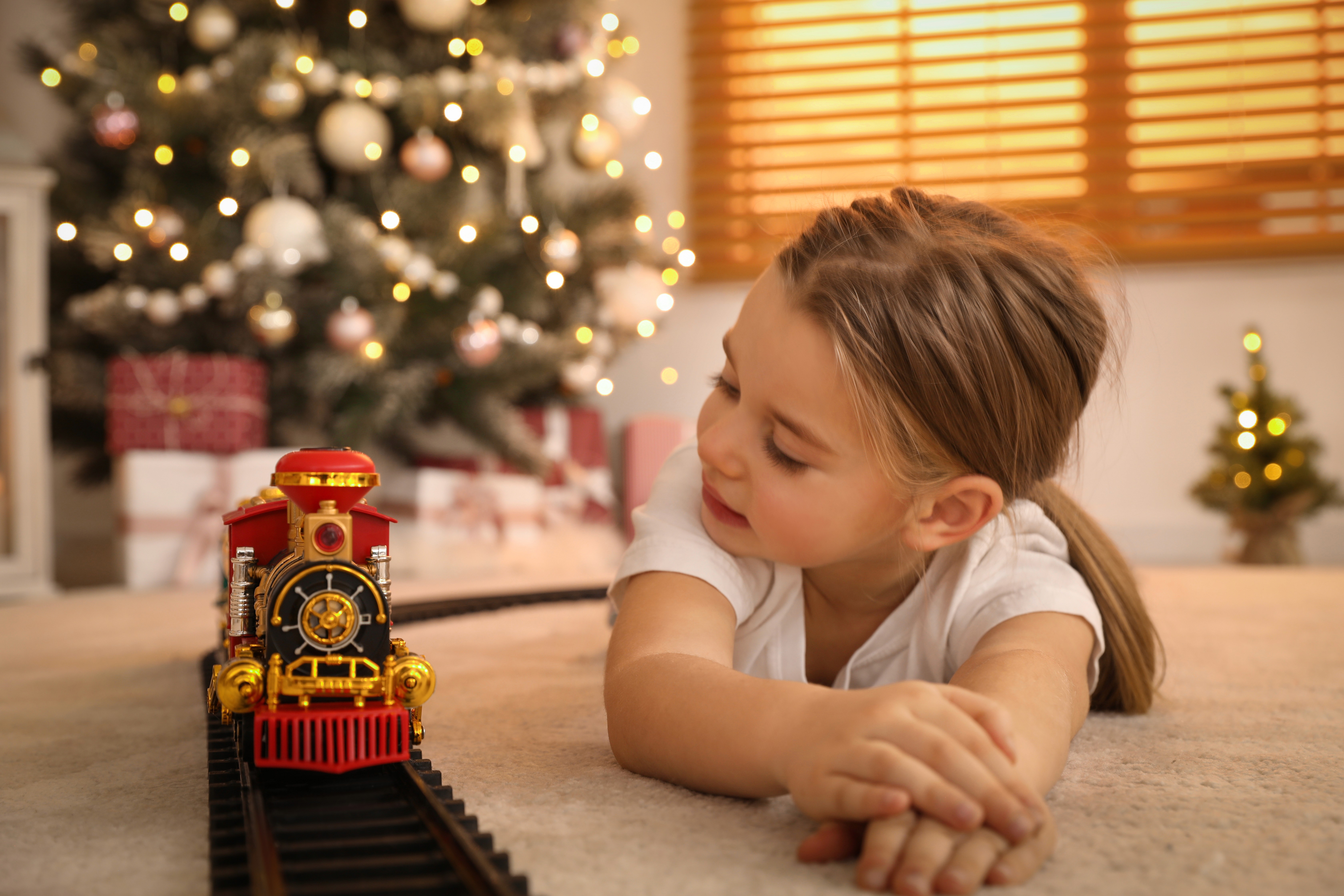 Young child playing with a toy train set beside a Christmas tree and holiday gifts, representing how divorce affects holiday custody schedules and parenting time arrangements in Massachusetts