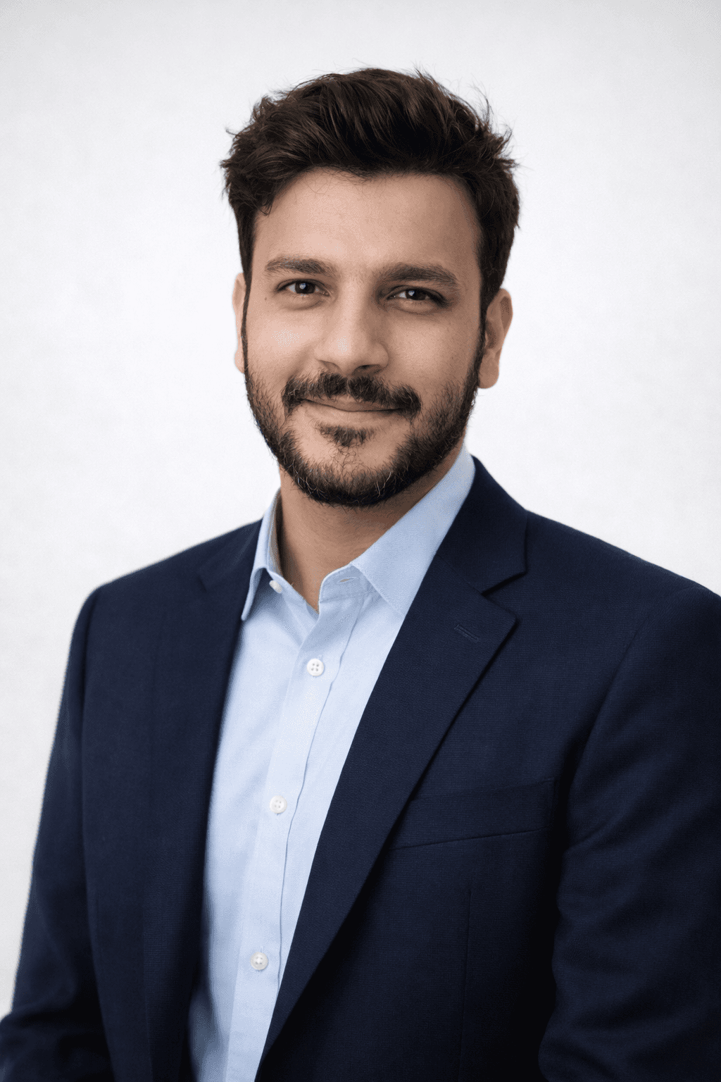 Young man in a dark suit jacket and cream sweater vest over a blue shirt with a patterned tie. Professional and confident expression, neutral background.