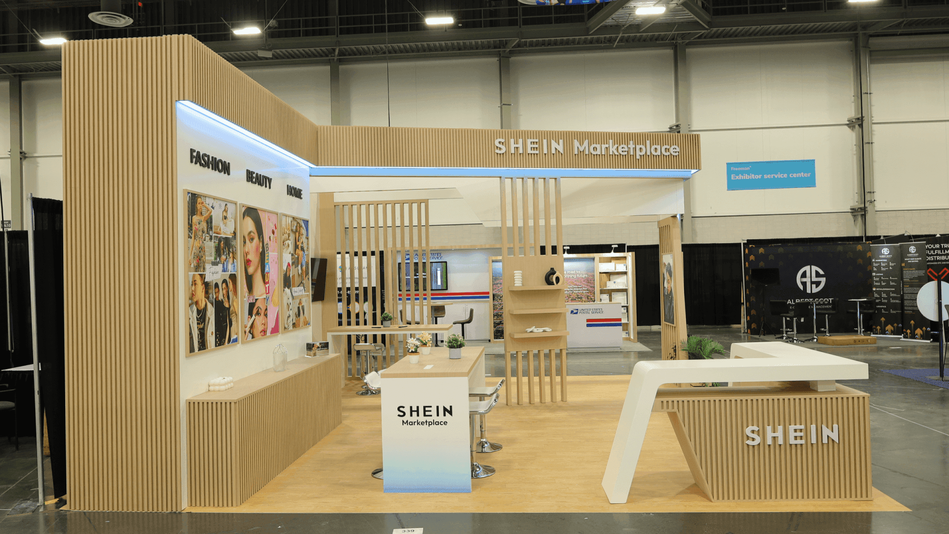 Side view of SHEIN Prosper Show 2025 20x20 retail booth with blue brand wall, overhead hanging sign, open discussion area, and category display graphics