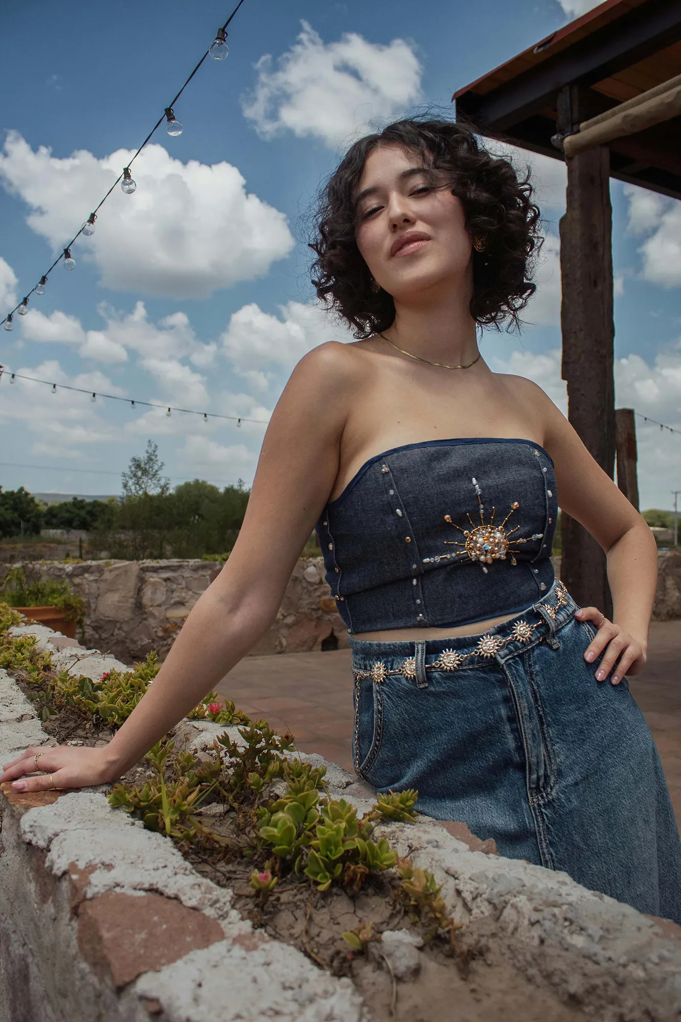 A woman poses outdoors in a sunburst-embellished denim top