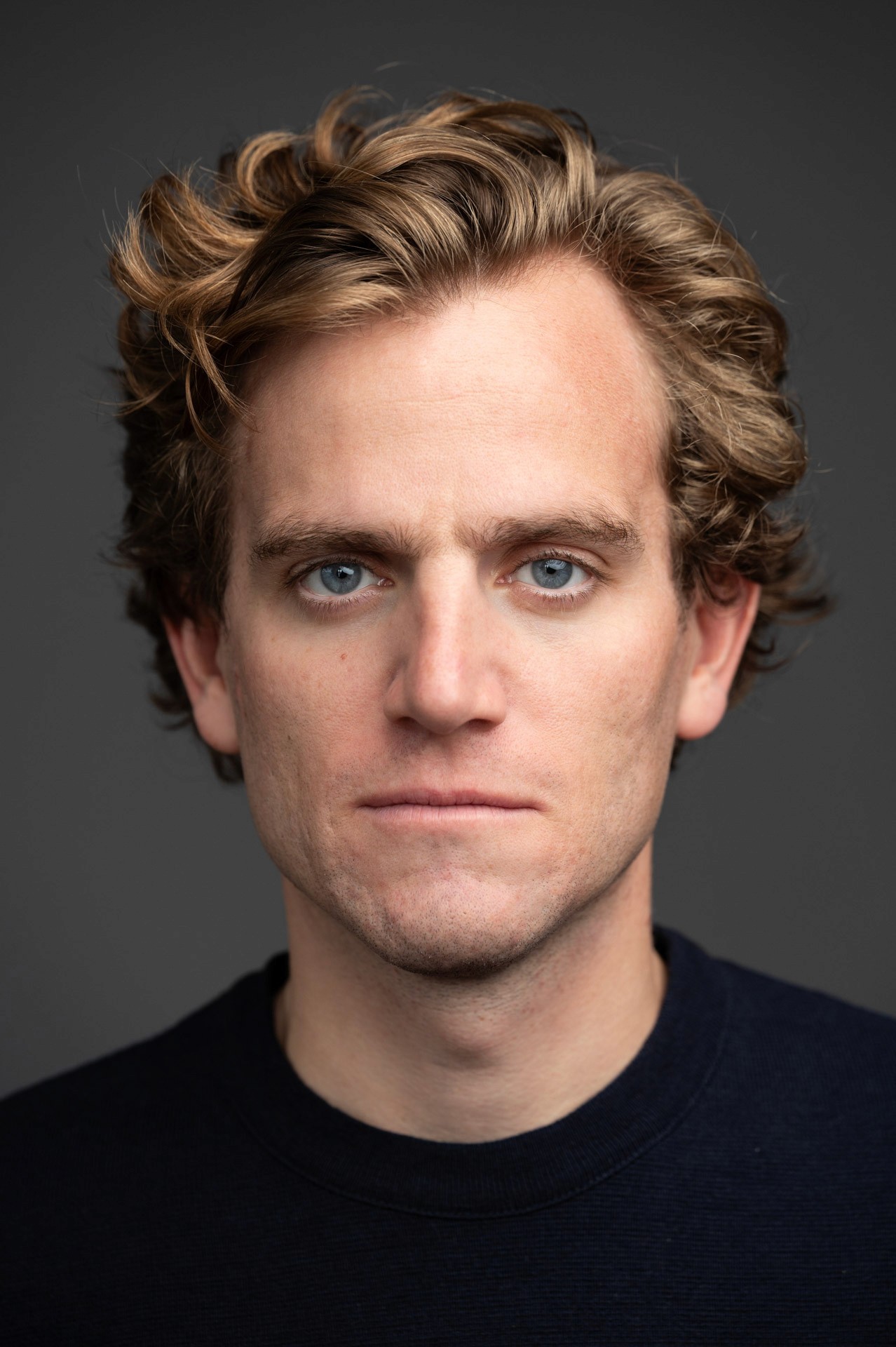 comedien aux yeux bleus et blond avec un pull noir