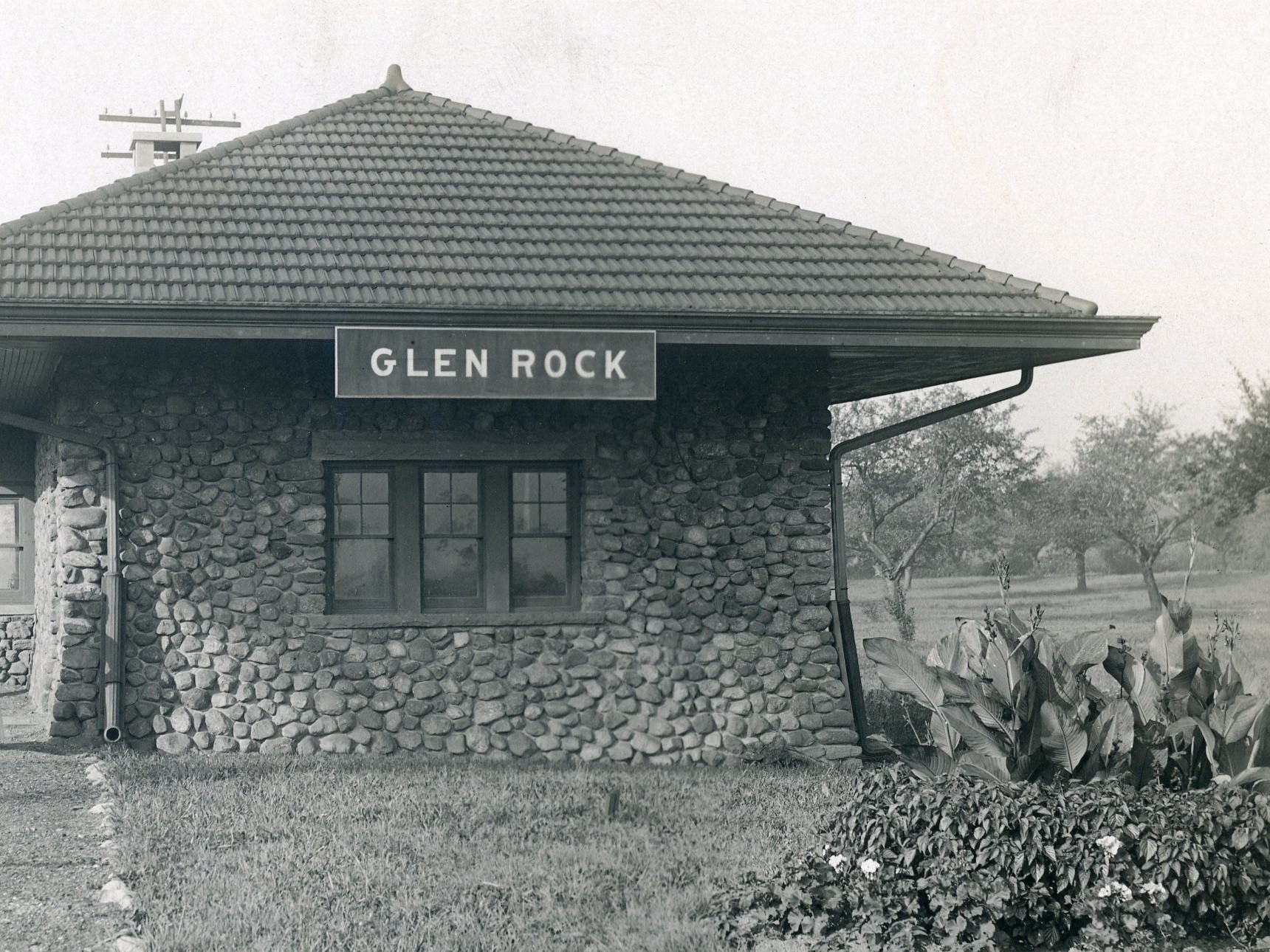 Historic black-and-white photograph of the Glen Rock Main Line station with a GLEN ROCK sign above the stone facade in Glen Rock, New Jersey.