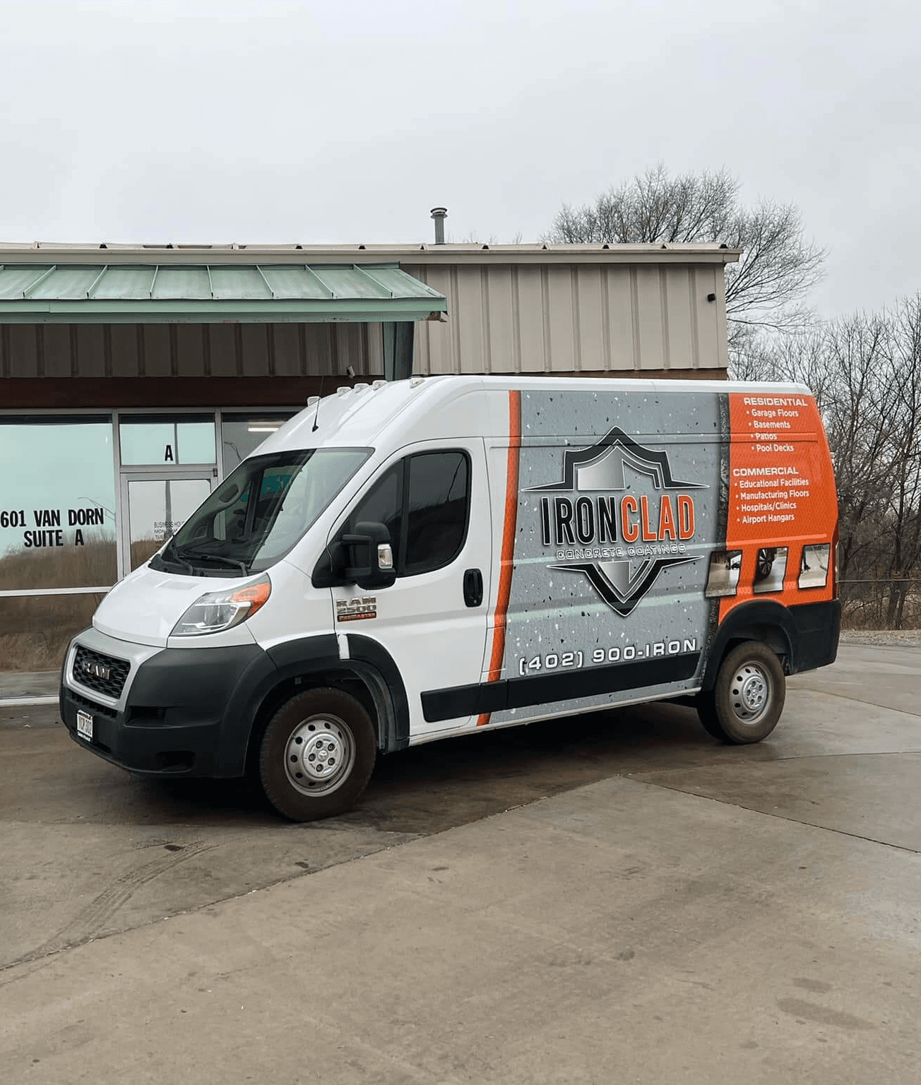 A white commercial van with "Iron Clad" branding is parked in front of a brick and metal industrial building.