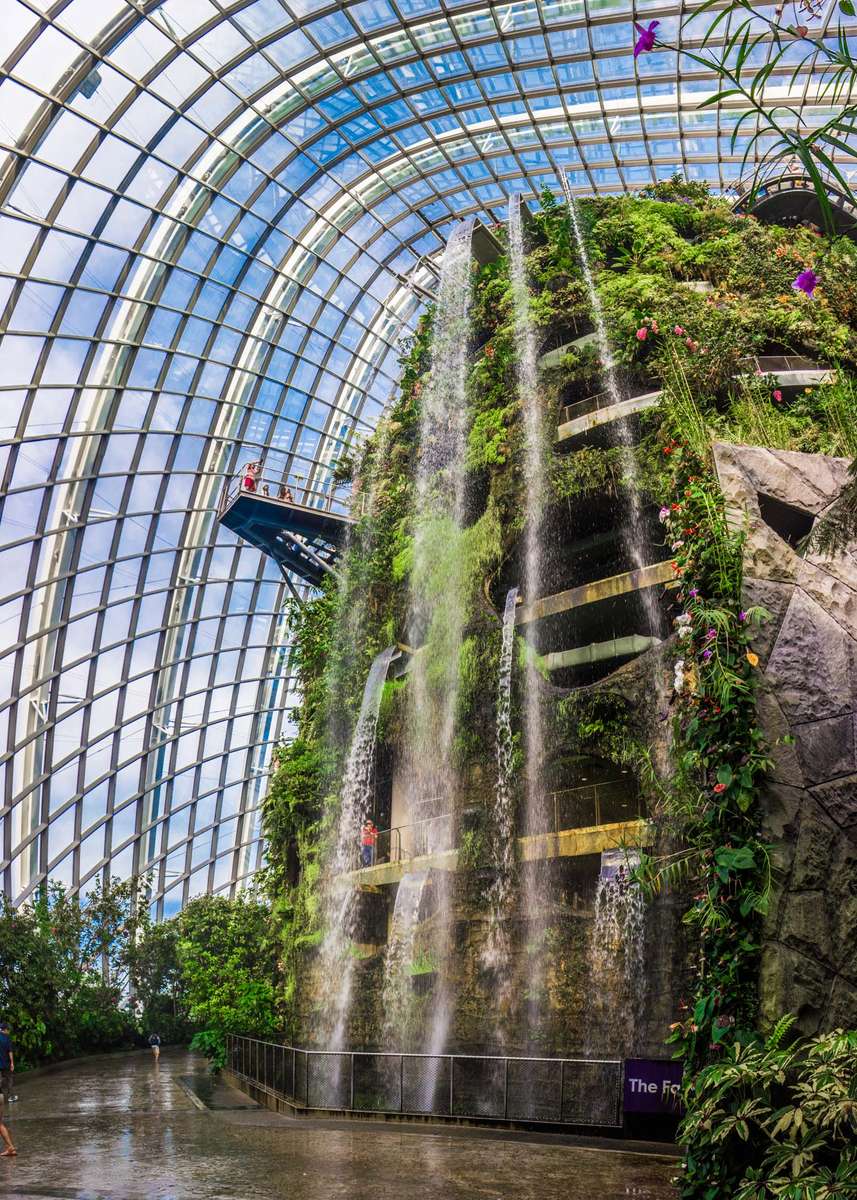 A massive indoor waterfall and lush green garden wall under a glass and steel dome structure with a nearby sign.