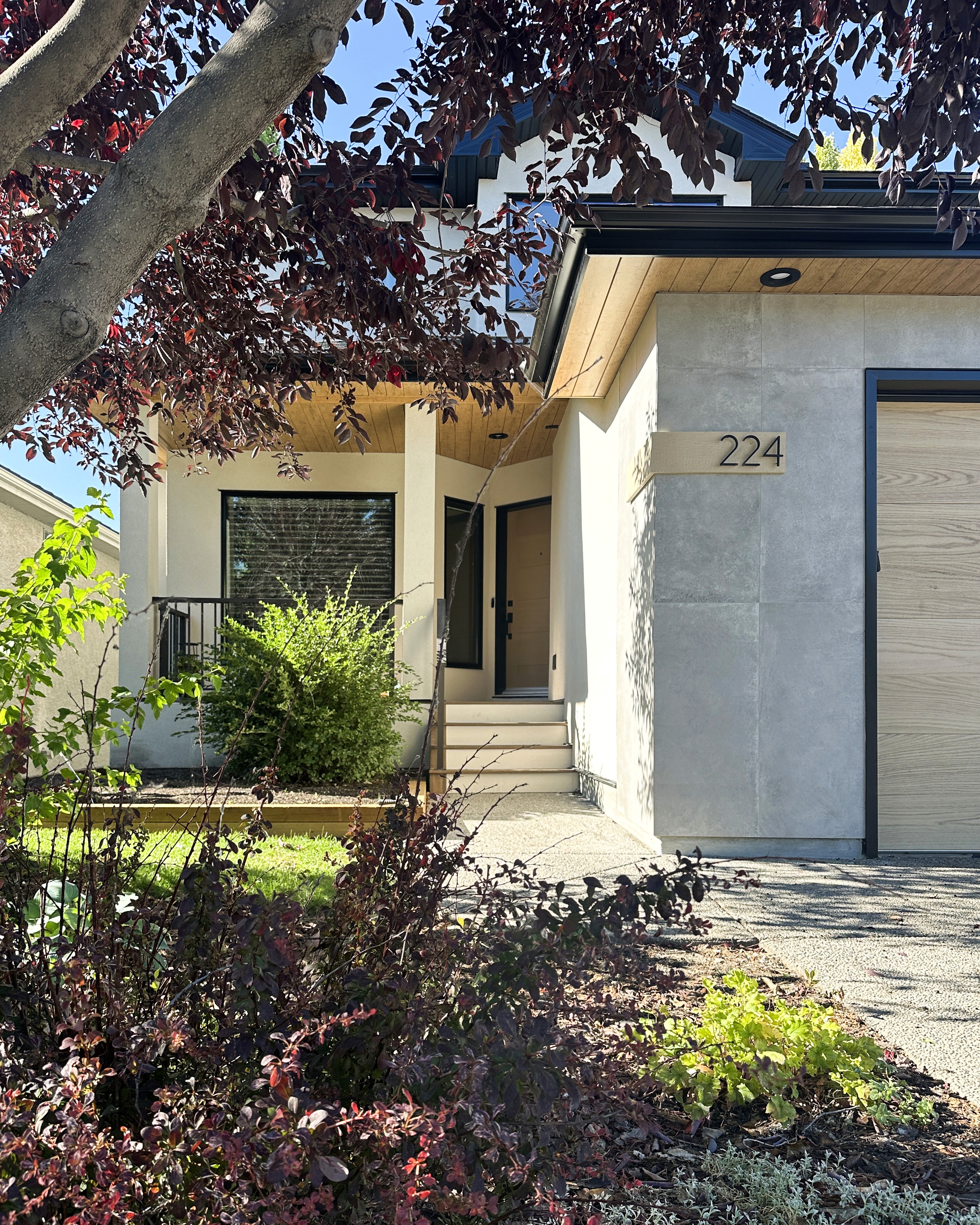 Image of Modern home exterior with gray stone facade, wooden accents, and lush garden by KHD Homes builder.