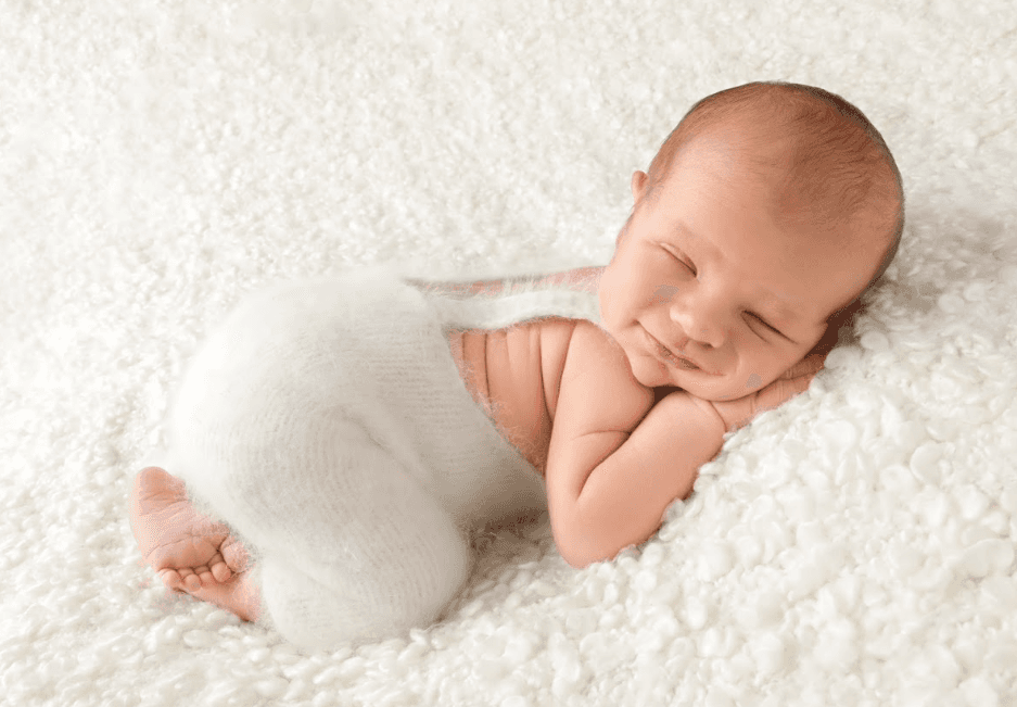 A baby smiling in his sleep while lying flat on his tummy on a plush, wool blanket.