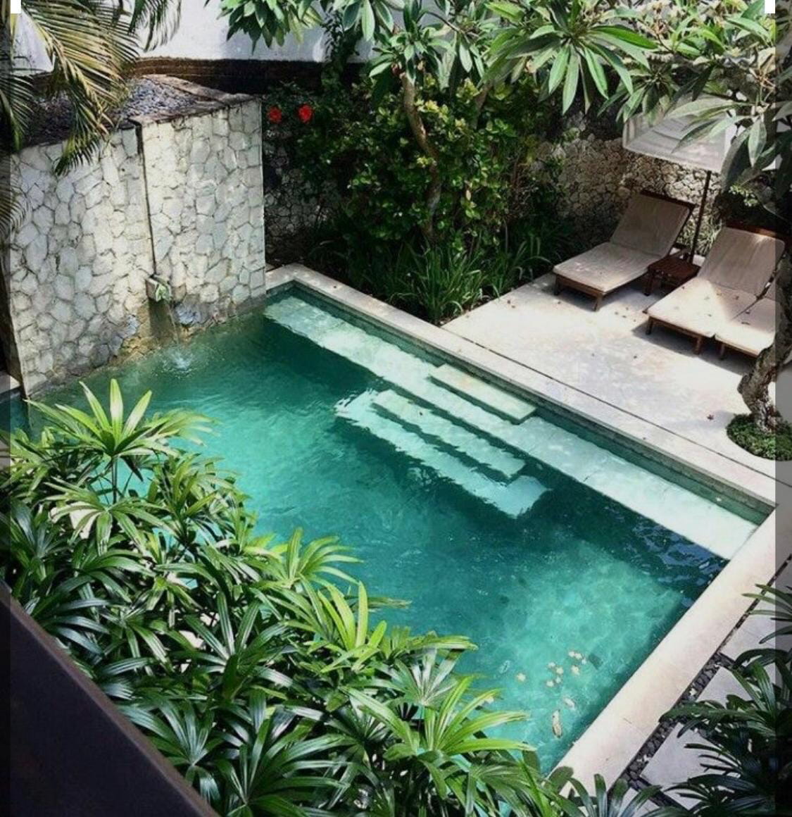 Exclusiva piscina revestida en Piedra Bali verde esmeralda, con una pequeña cascada sobre muro de piedra y reposeras de madera en patio interior.