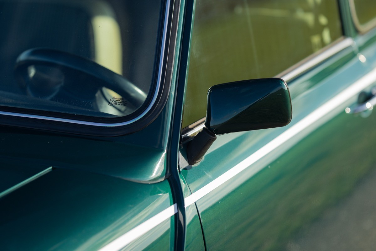 Close-up view of a green car's side mirror and door, reflecting light and showcasing its sleek lines.