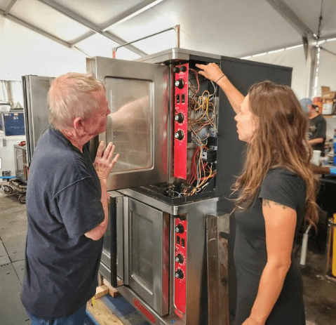 A man and a woman inspect a piece of equipment inside a tent, discussing its features and functionality.