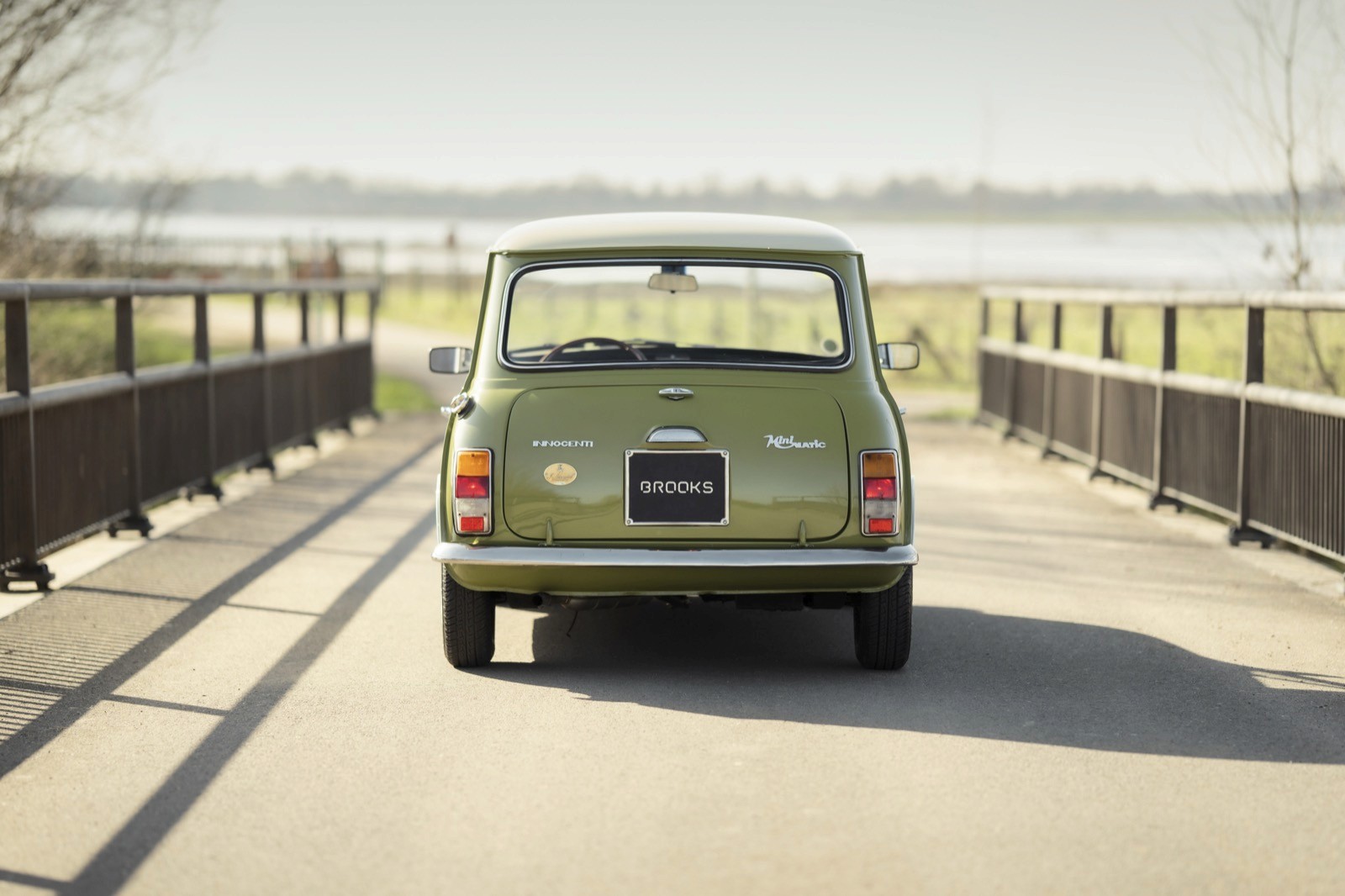 A vintage green van parked on a bridge, with a serene landscape in the background.