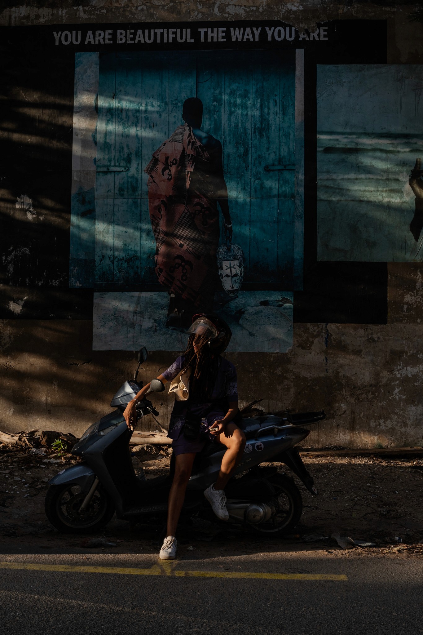 A young person wearing silver sports sunglasses lies on their stomach on a patterned rug, resting their chin on their hands while looking at an open magazine.