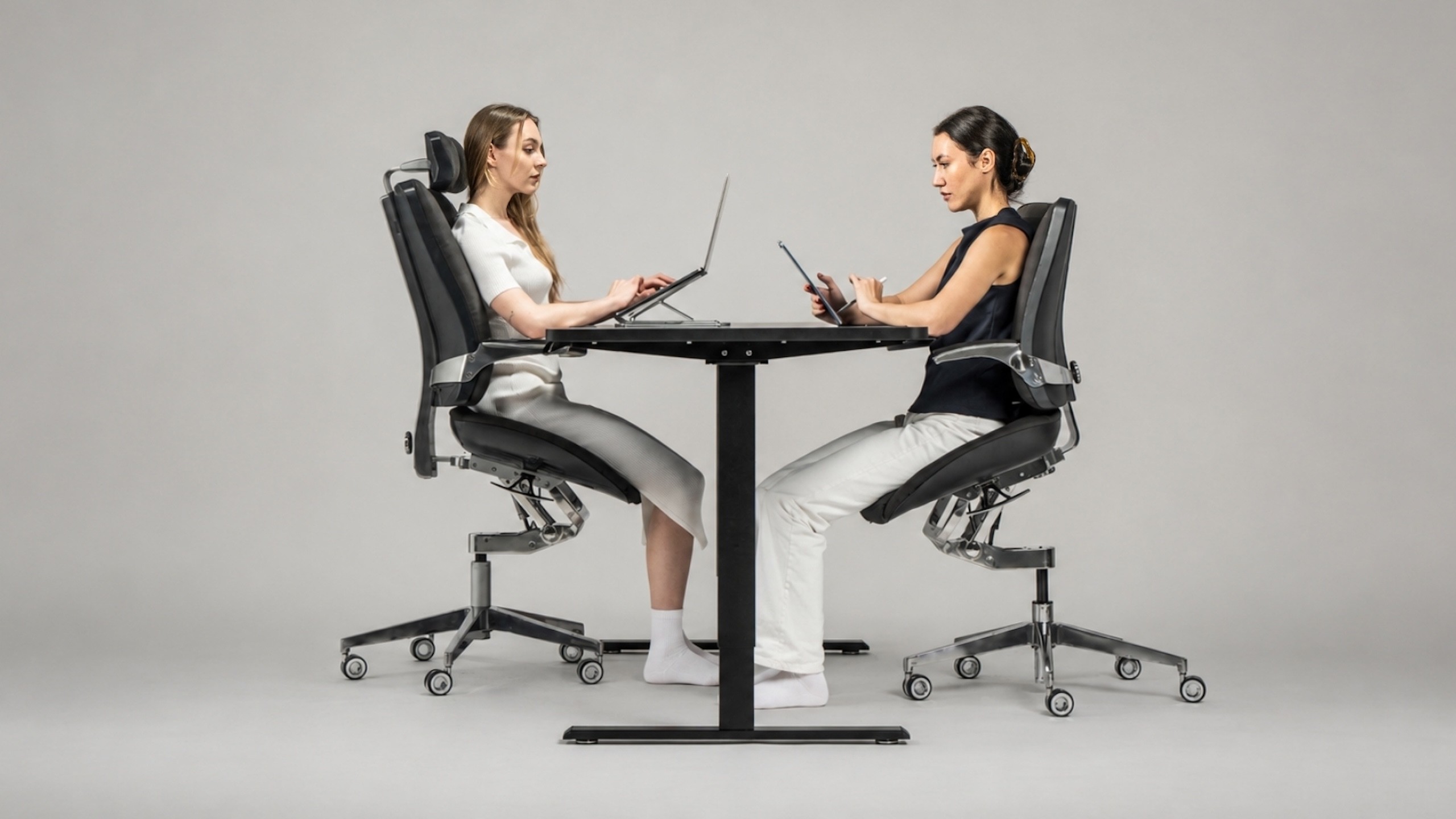 Two professionals work comfortably across a shared desk while seated in Levitask Vision ergonomic chairs.