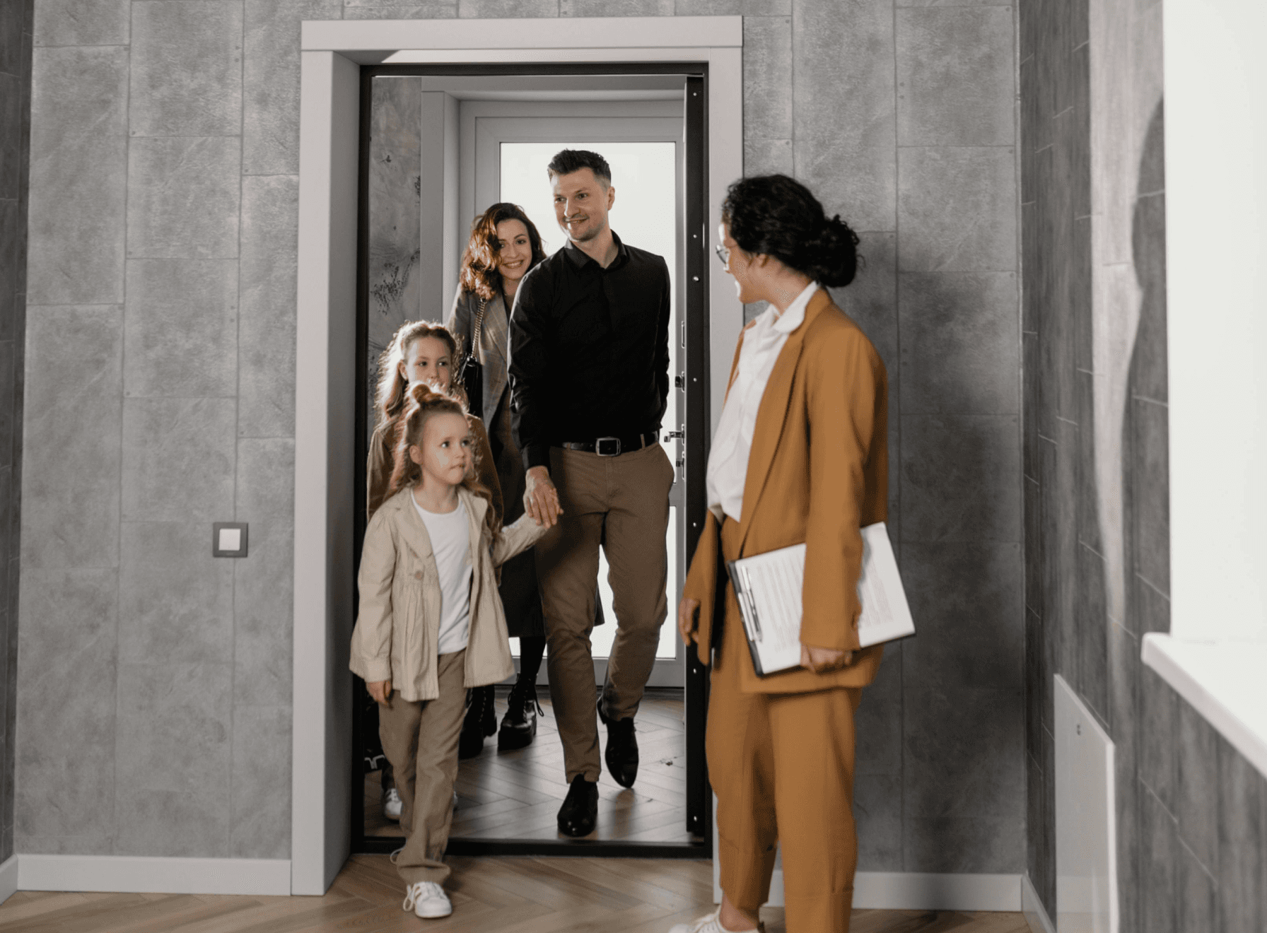 A family with a child stands in an entryway, greeting a woman in smart casual attire.