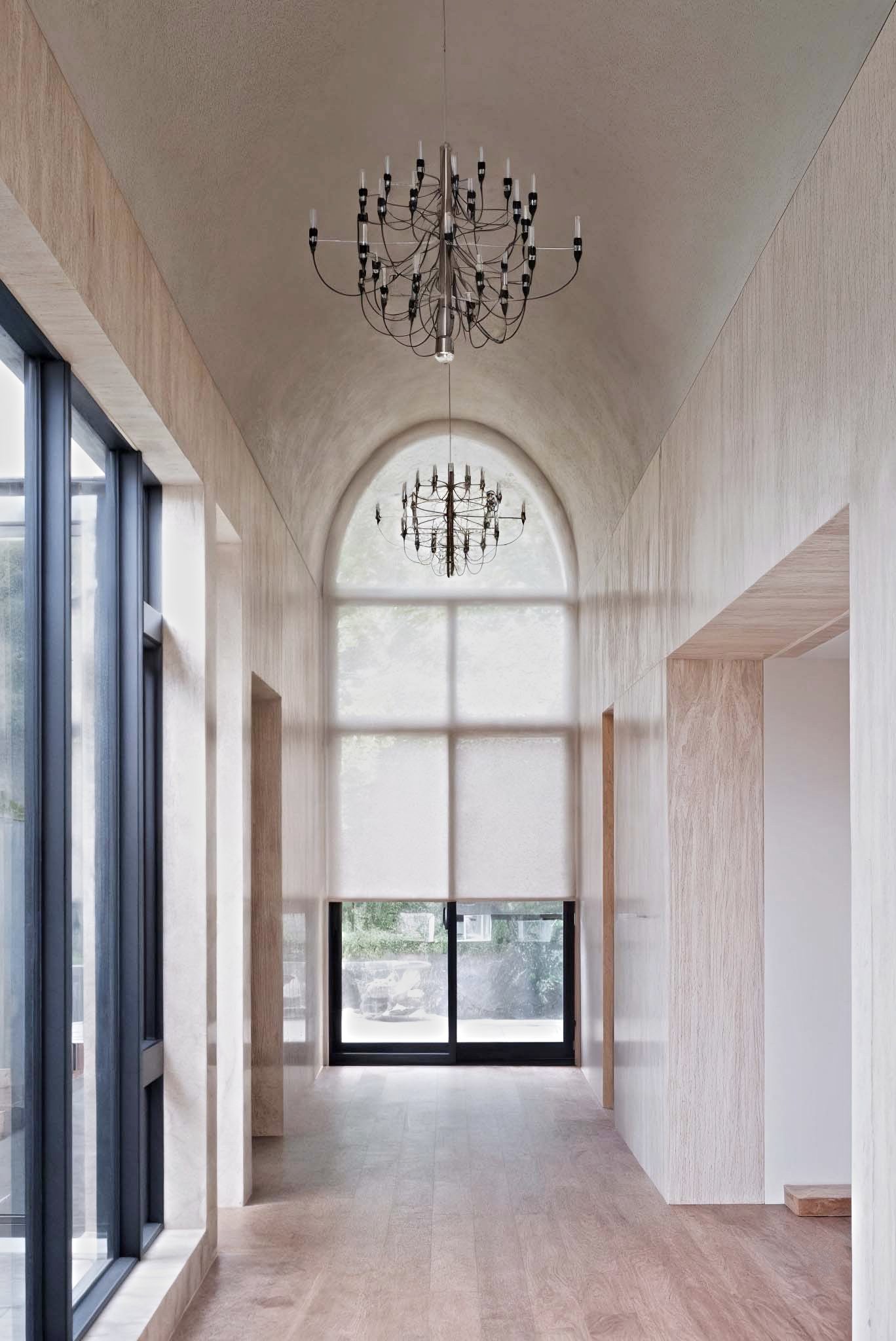 高拱形天花與吊燈設計的走廊空間，光線透過大片紗窗灑入，牆面與地板使用溫潤木質材料