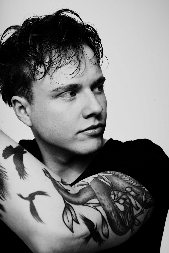 Black-and-white image of the young man looking to the right with focus on tattooed upper arm