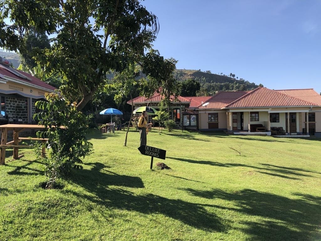 A wide green lawn with a "Deluxe Rooms" sign in front of several single-story guest houses.