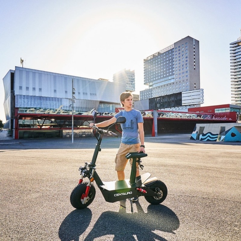 Jeune homme debout à côté d’une trottinette électrique Centauro 2000W avec siège dans un cadre urbain contemporain