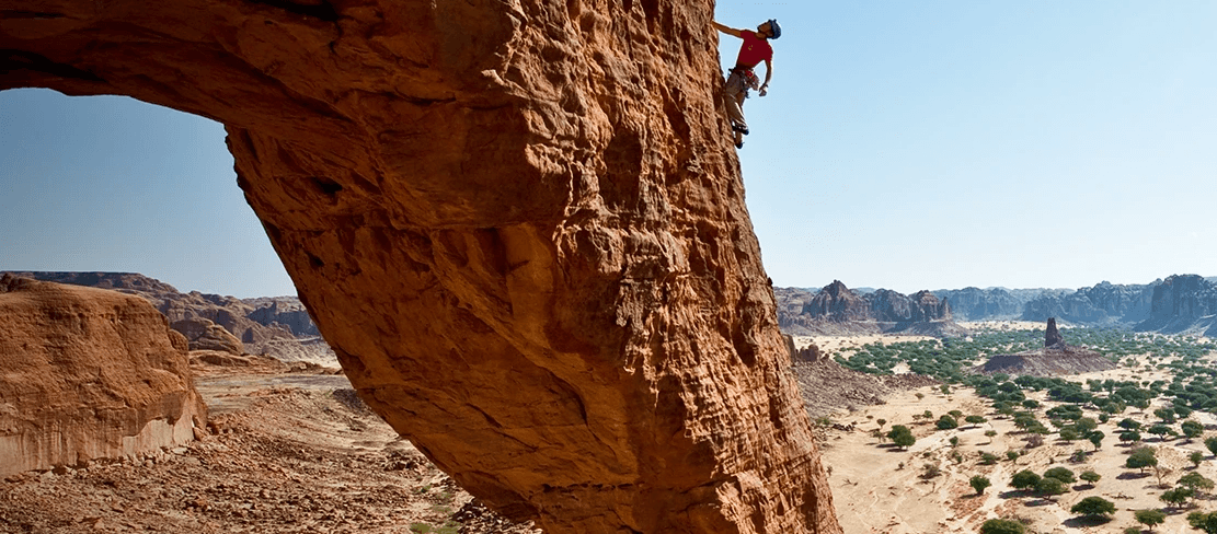 A climber pauses on a rock face to visualize their route on a unique rock formation in the country of Chad in northern Africa.