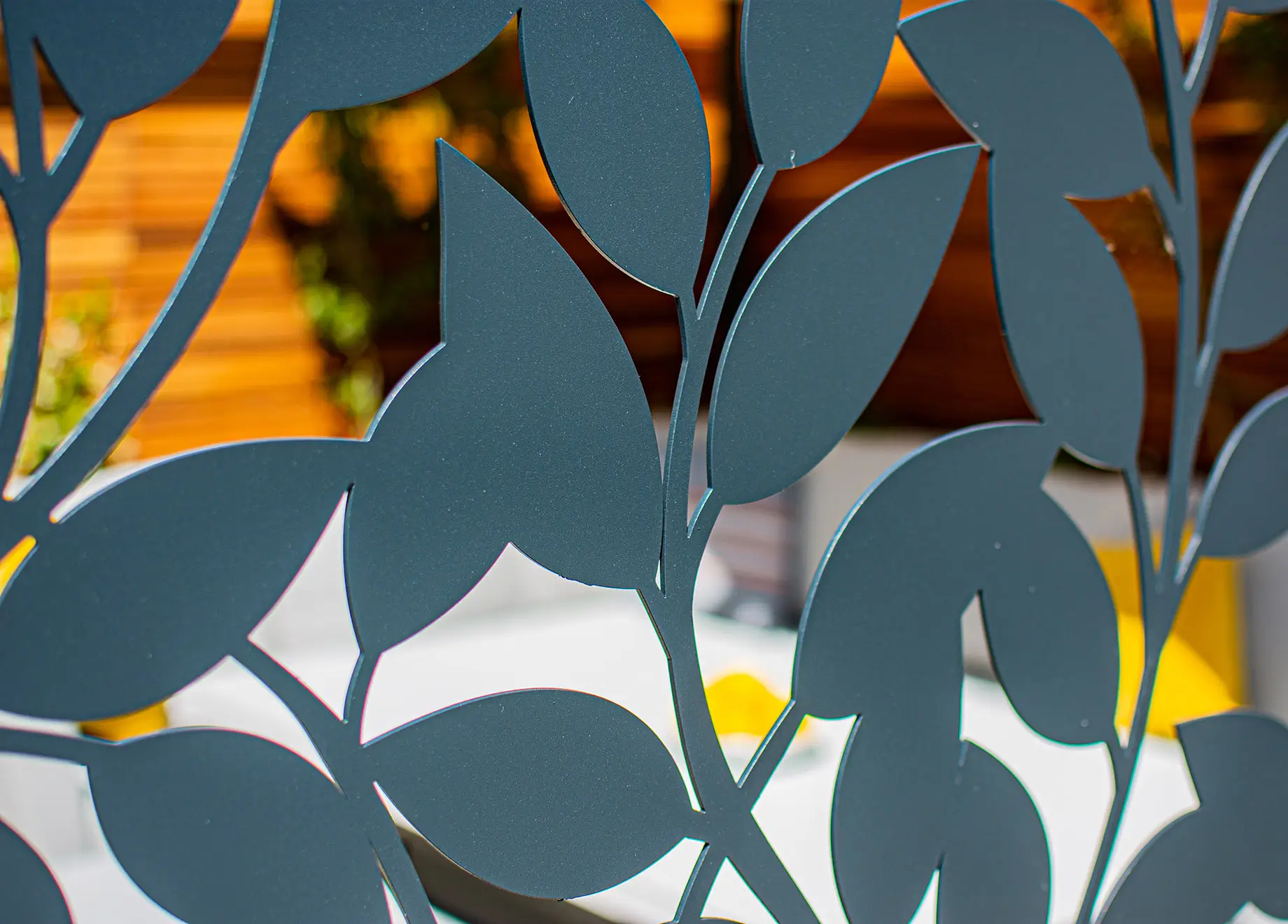 A close-up of decorative leaf patterns in dark metal, casting shadows against a colorful, blurred background.