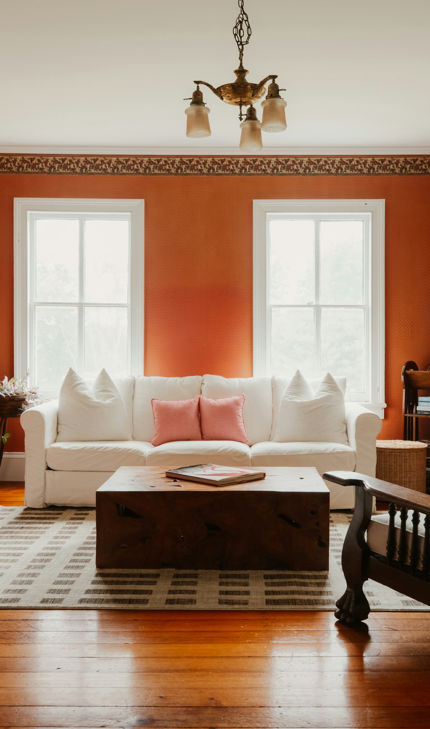 Bright, lived-in living room with terracotta walls, a wooden floor, a white sofa and two tall windows.