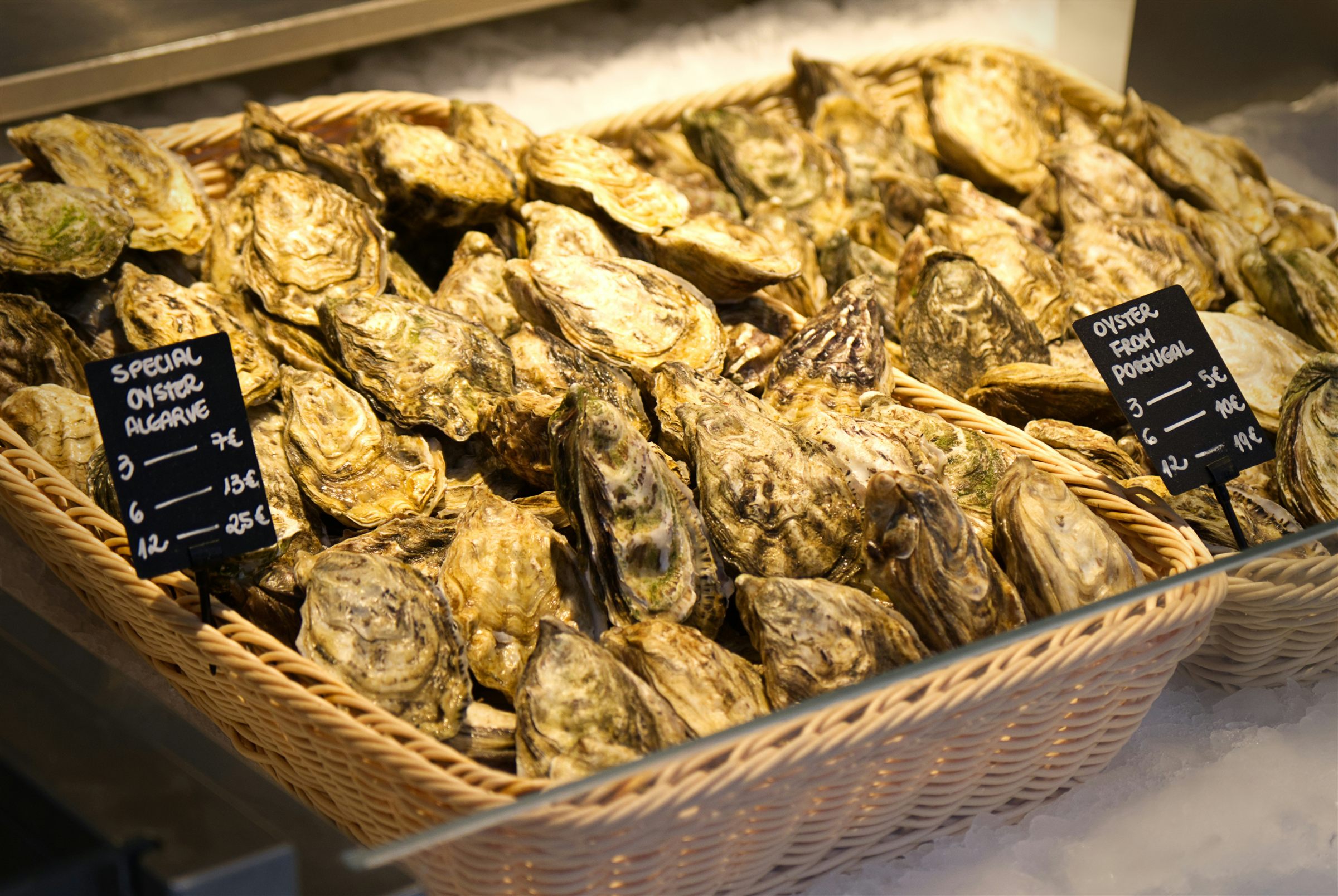 Oysters piled in a basket on ice with handwritten chalk labels