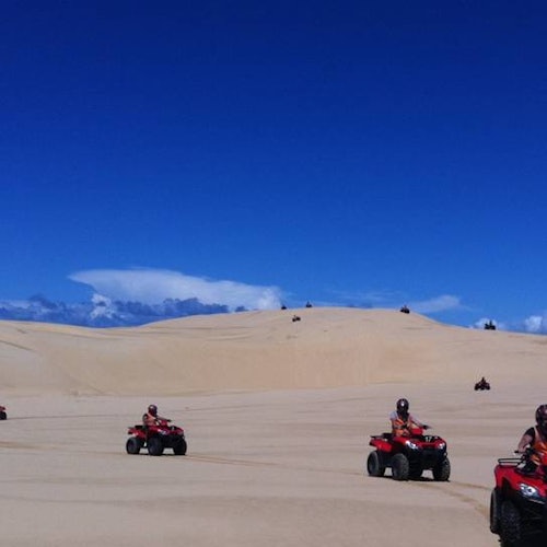 人们在明媚的蓝天下，骑着红色的全地形车穿越广阔的沙漠。