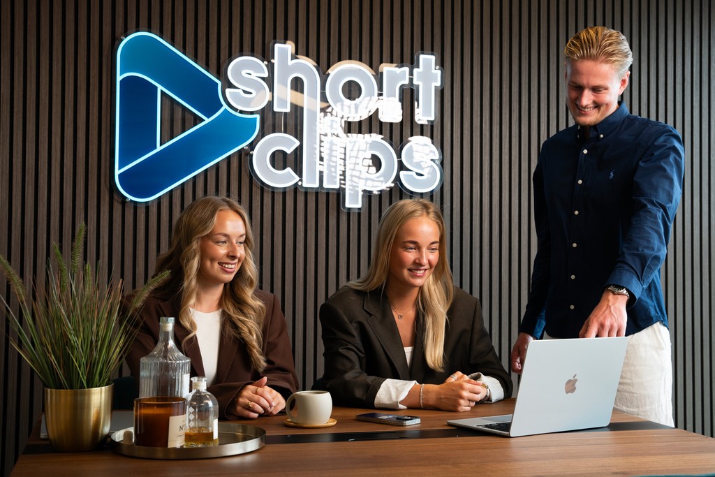 Het Shortclips-team aan tafel op kantoor voor de logowand
