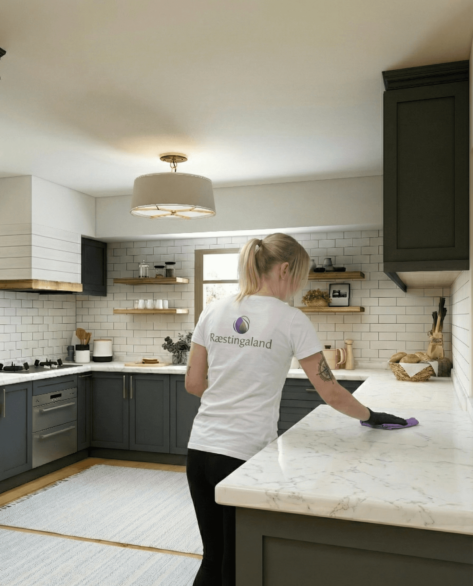 Starfsmaður Ræstingaland að þurrka af eldhúsborðplötu í nútímalegu eldhúsi.