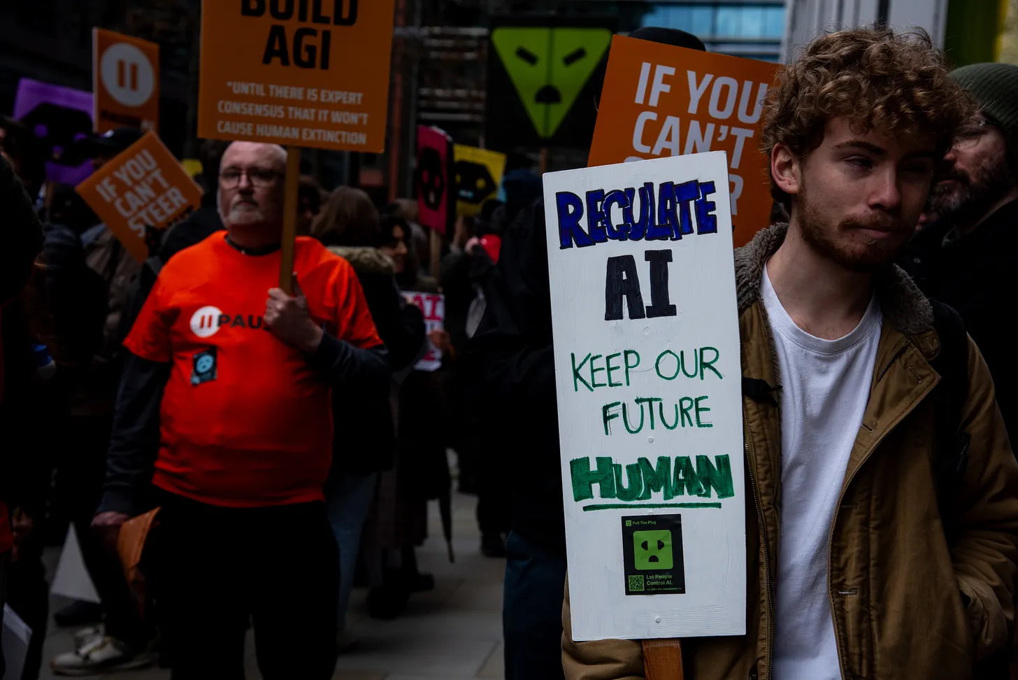 Protesters carrying signs calling for AI regulation, including “Regulate AI. Keep our future human.”