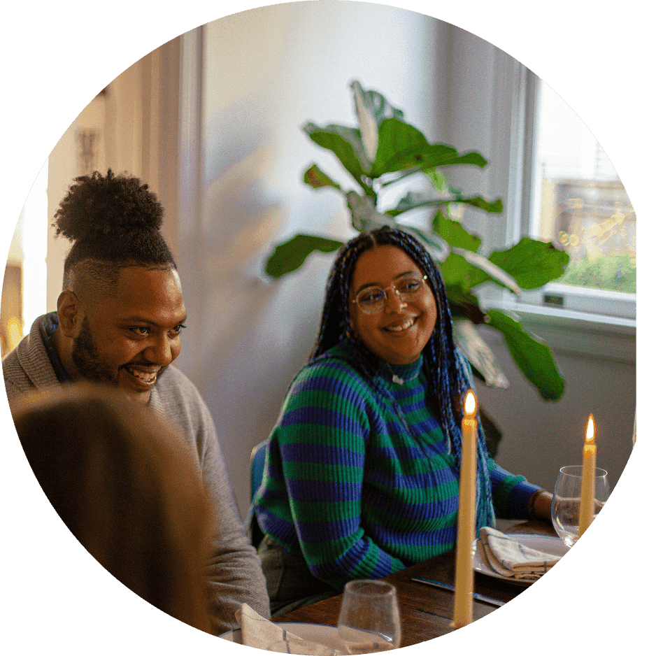 A group people sit at a dining table with lit candles, smiling and chatting over a meal