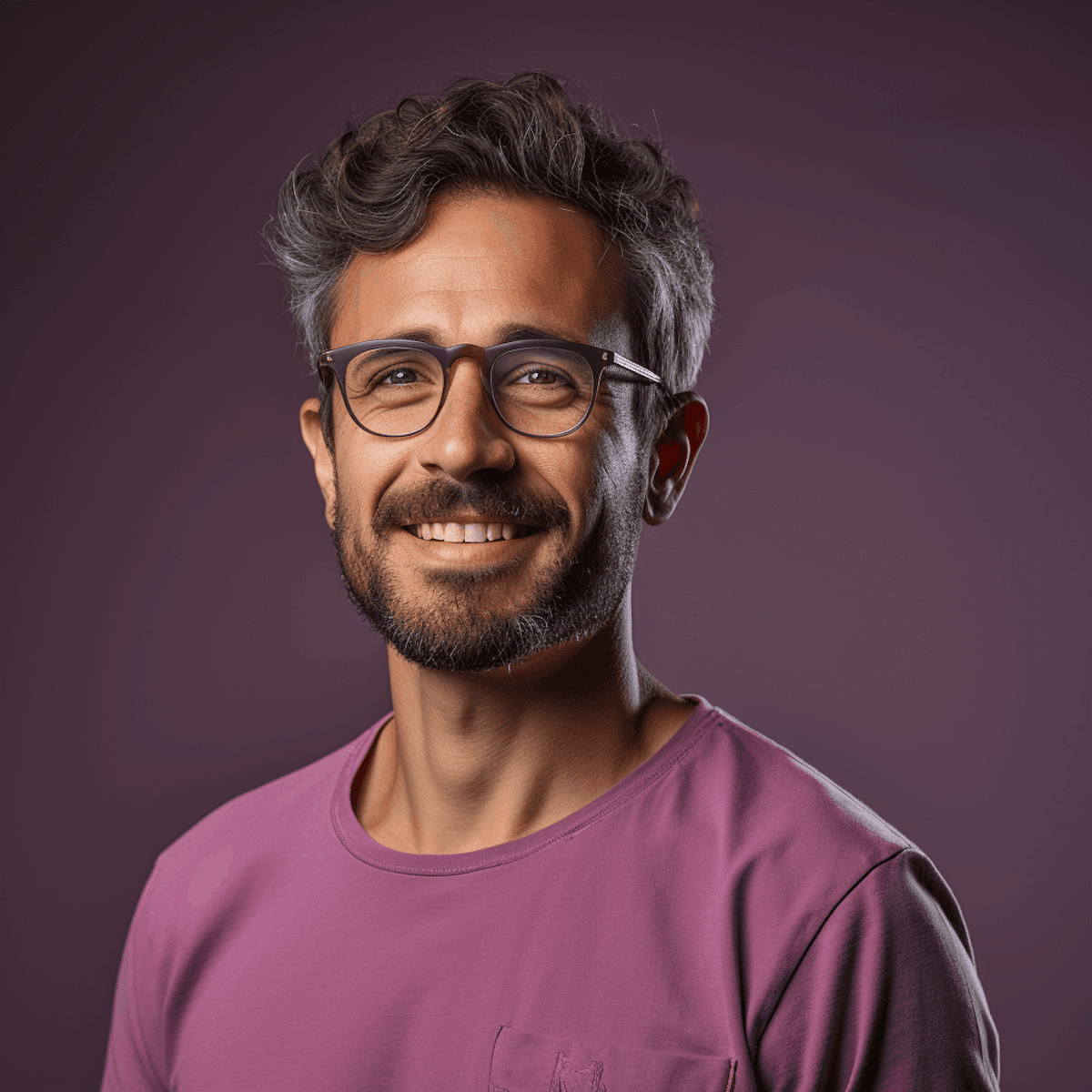 Smiling man with glasses and a beard in a purple shirt, set against a matching purple background. His expression conveys warmth and approachability.