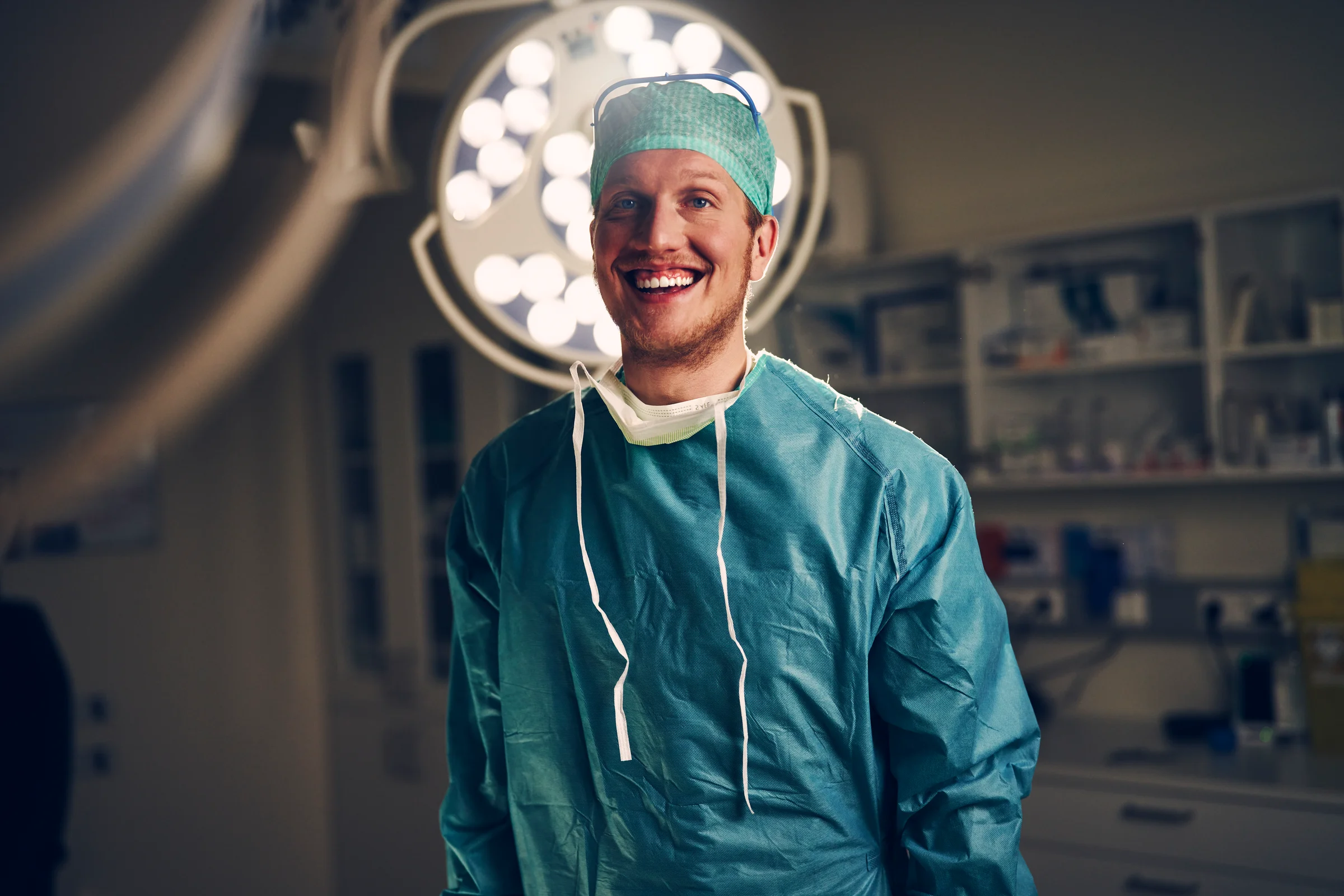 A smiling healthcare professional wearing surgical scrubs and a cap in a well-equipped operating room, representing careers in Iceland’s healthcare sector.