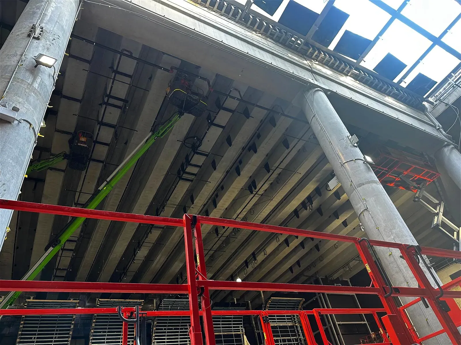 Workers in aerial lifts install lighting under concrete ceiling.