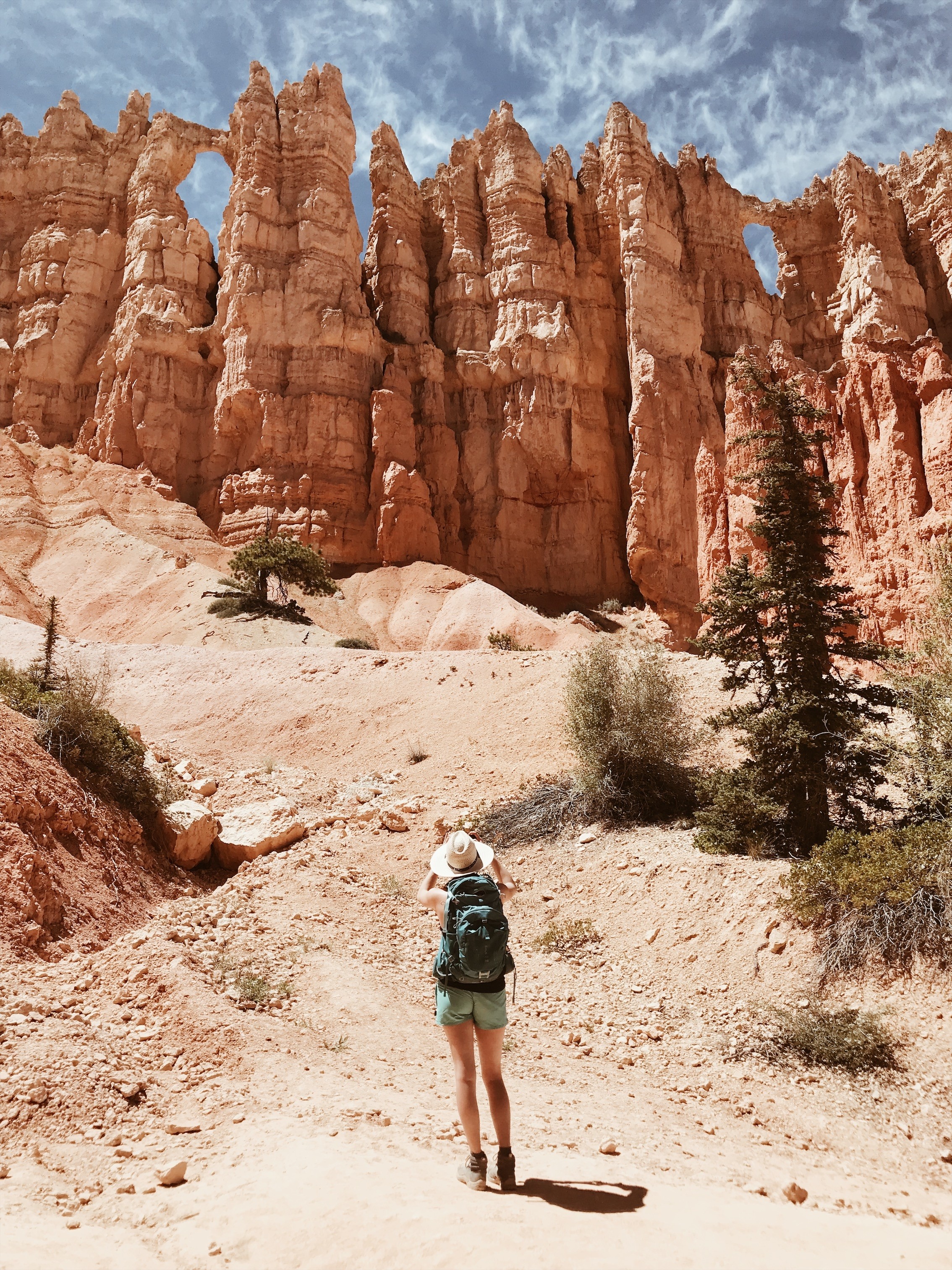 A hiker looks up at towering red rock formations.