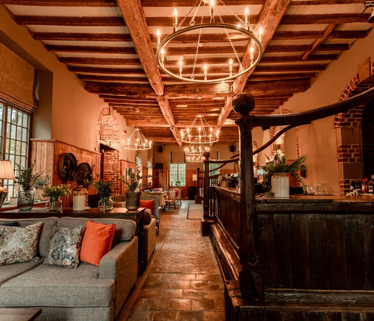 Outdoor restaurant terrace overlooking a tranquil lake at sunset. White tables and chairs are set with glassware. Sheer curtains add elegance. Calm ambiance.