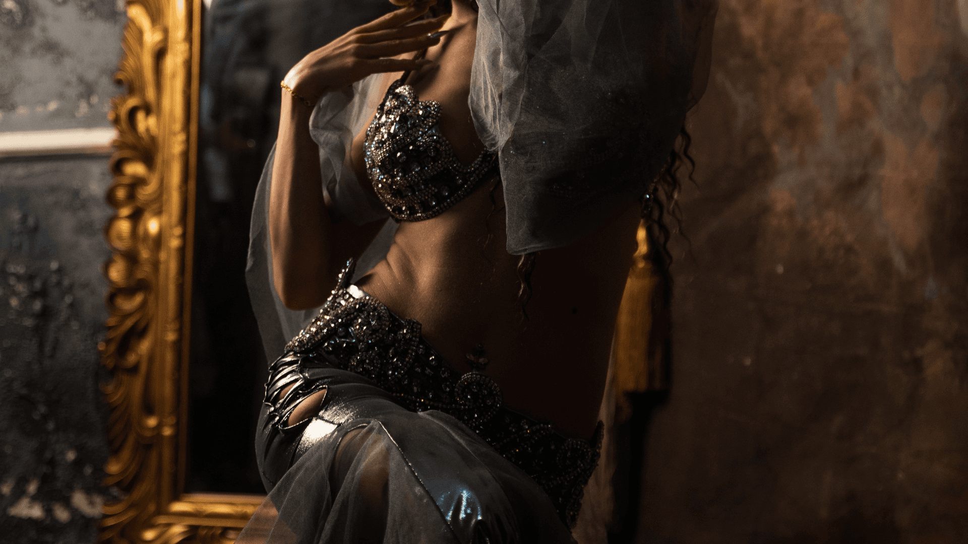 Close-up of a belly dancer’s shimmering silver costume, highlighting intricate beadwork and sensual movement, with a vintage mirror in the background.