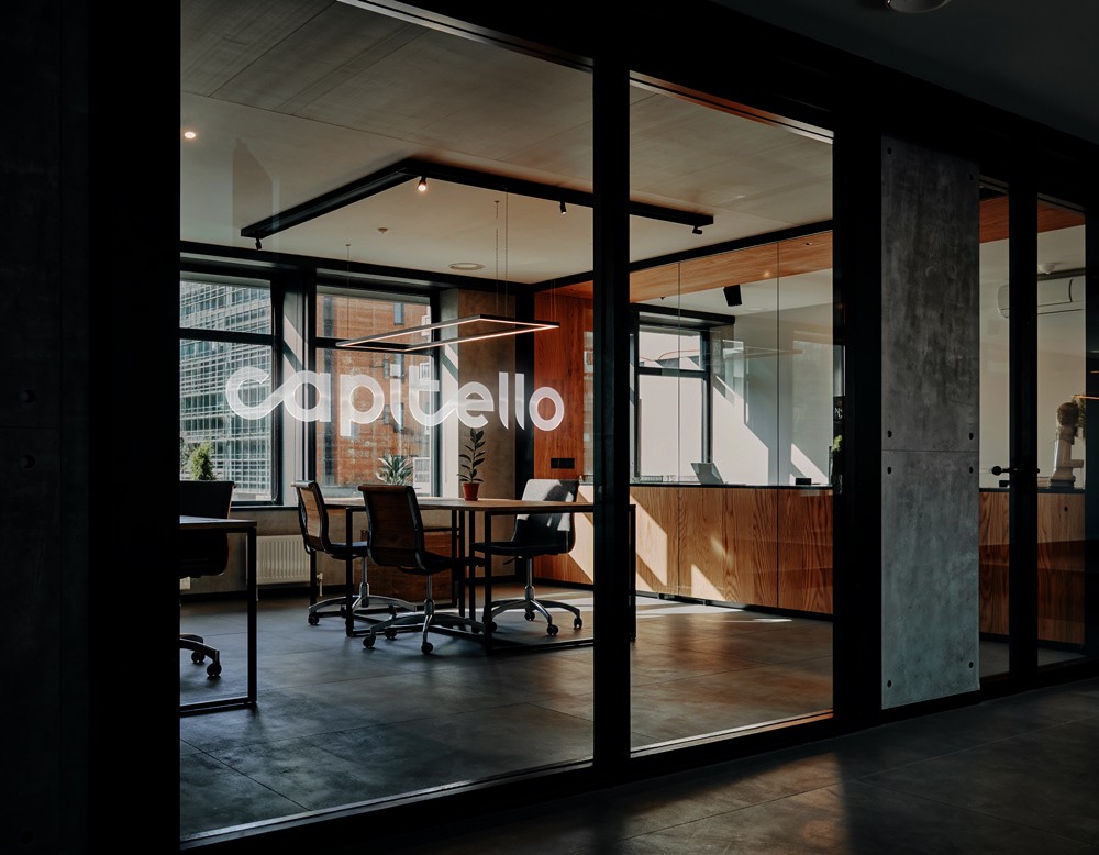 Modern office interior viewed through glass doors with the Capitello Finans logo applied to the glass partition, showing the brand identity in a professional workspace environment.