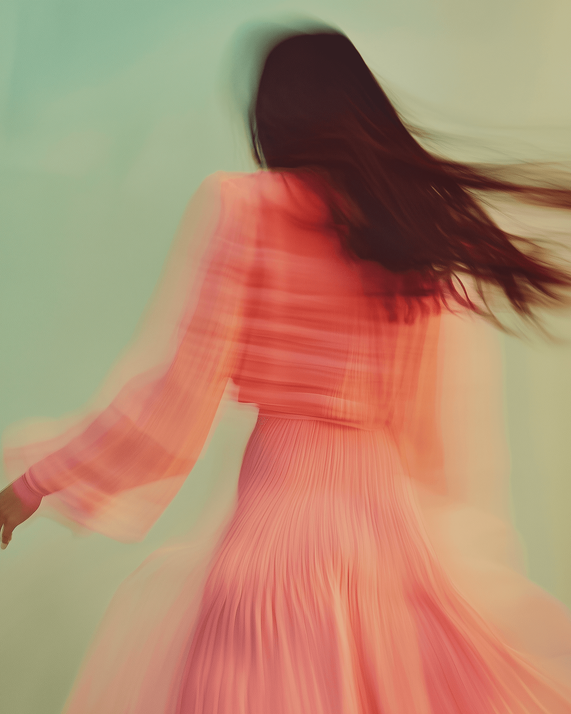 Performer with long dark hair in motion, wearing coral pink against a teal background.