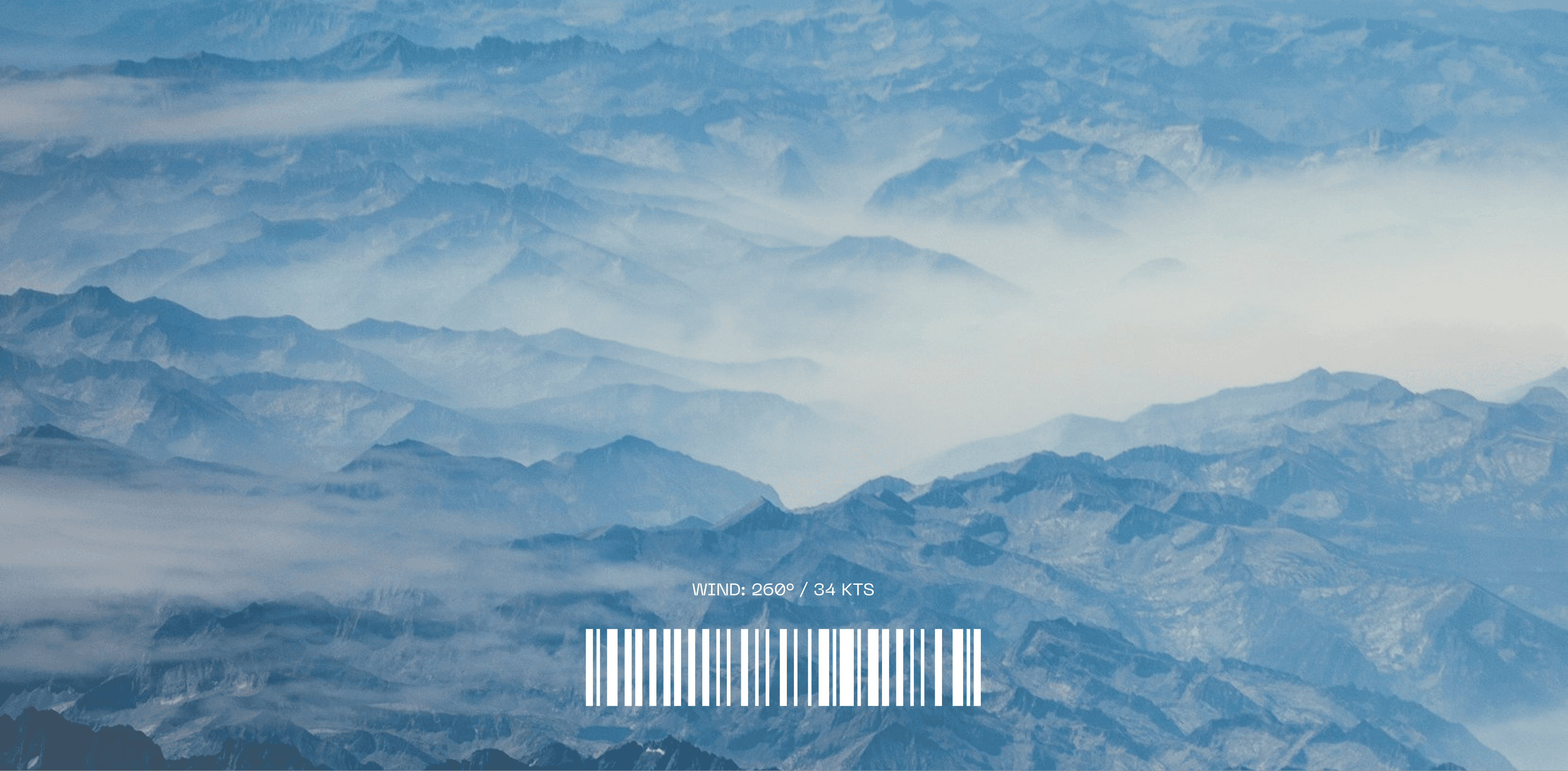 Aerial view of a vast, mountainous landscape covered in layered fog, with peaks emerging through the mist under a clear blue sky.