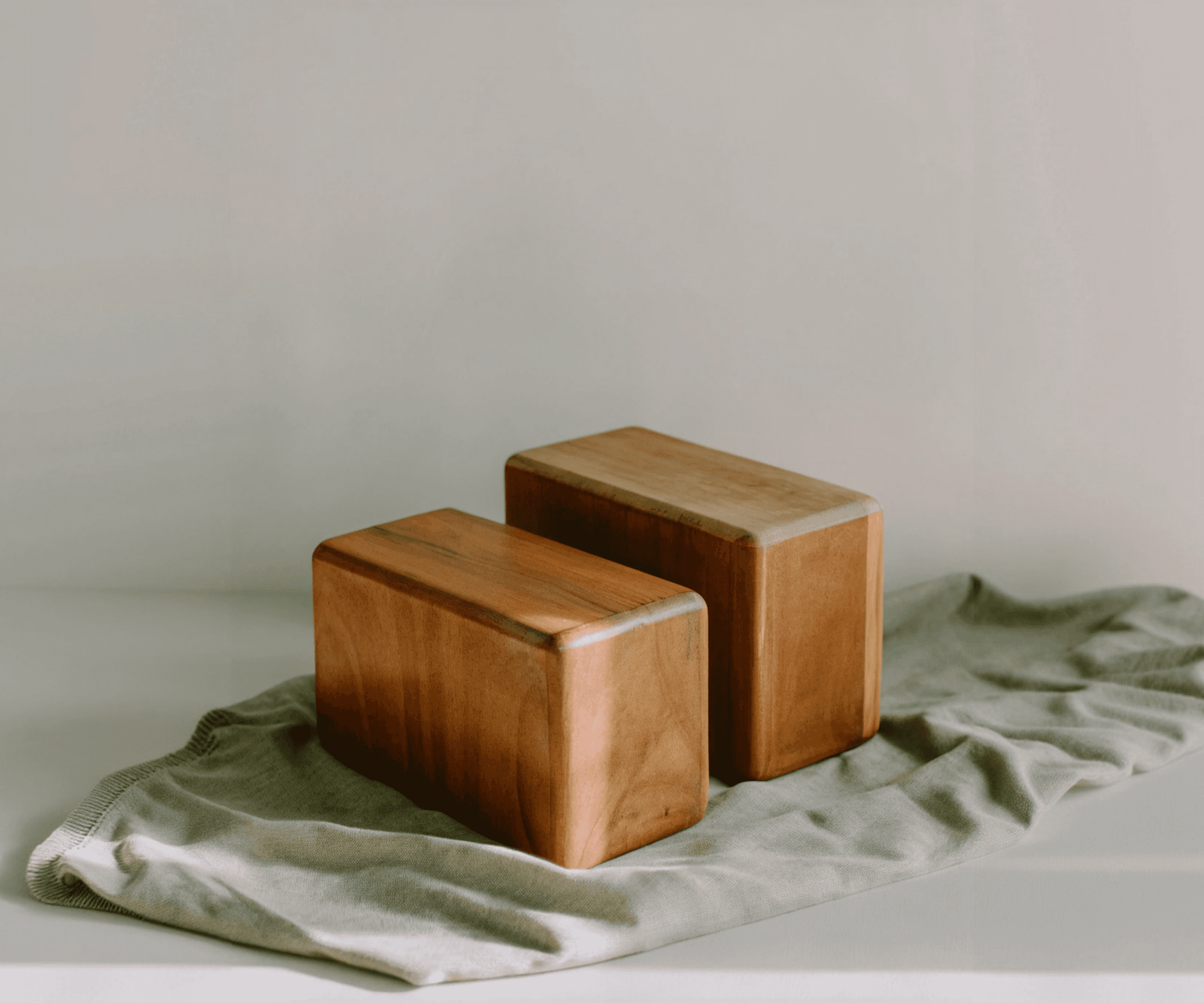 Two wooden yoga blocks on a sage green cloth against a light grey background