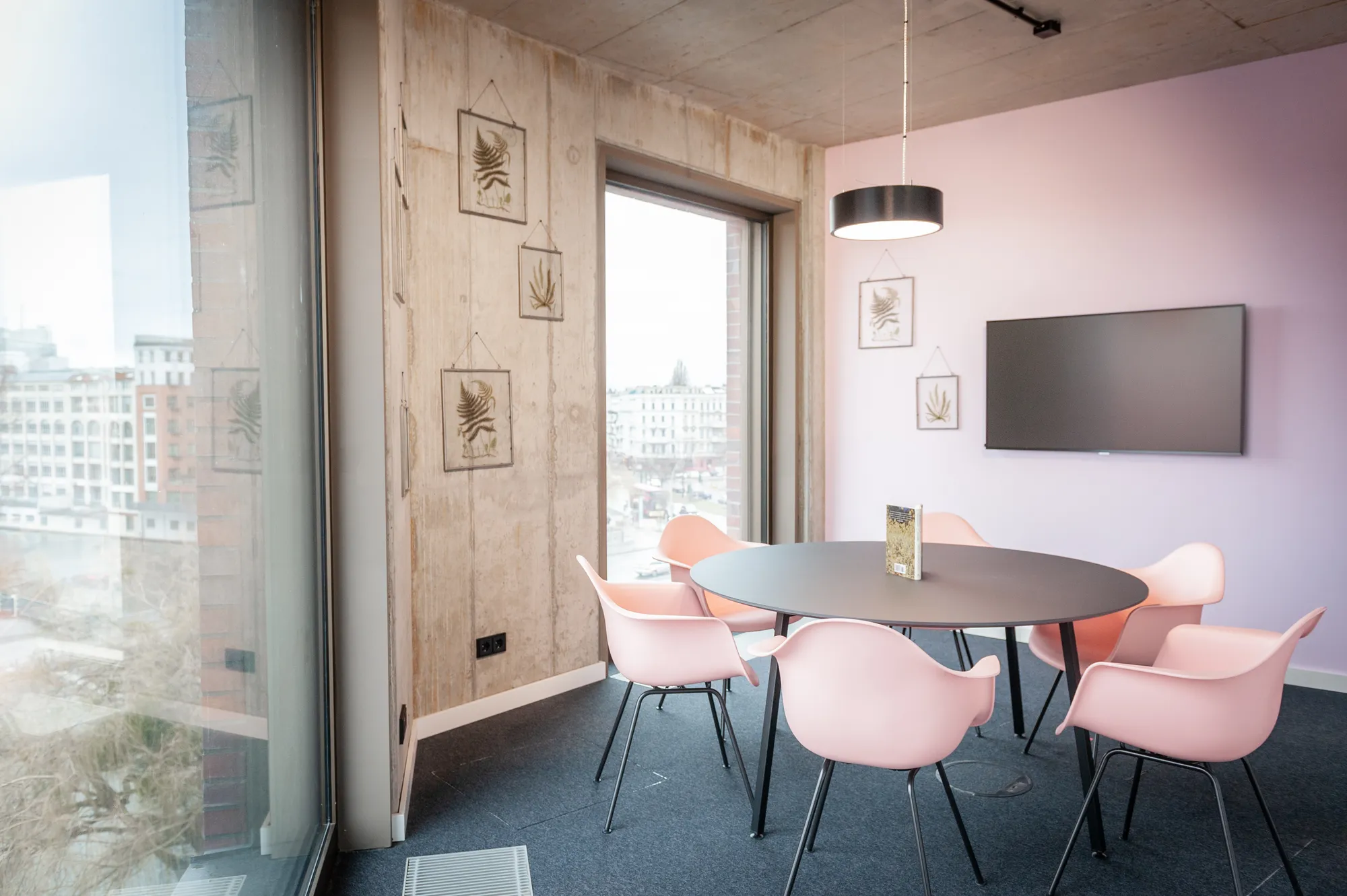 Meeting room with lilac wall, wooden panelling, round table with pink chairs and a screen.