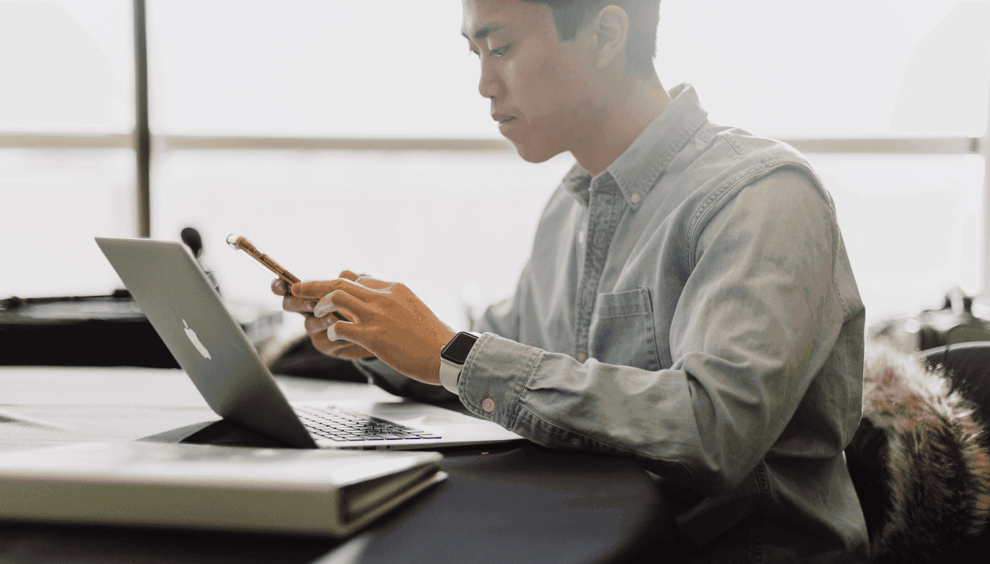 Man looking at phone and using computer